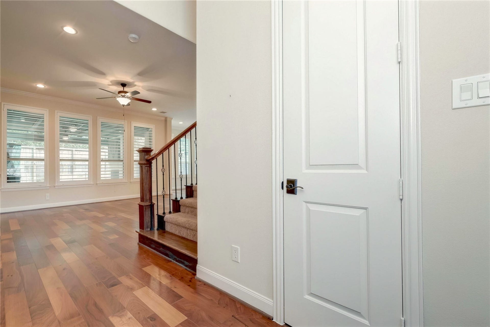 19 Herons Flight Place, Spring, TX 77389 Elegant hardwood floors lead into a spacious living area, highlighted by large windows and a stylish ceiling fan, with an inviting staircase featuring wrought iron details.