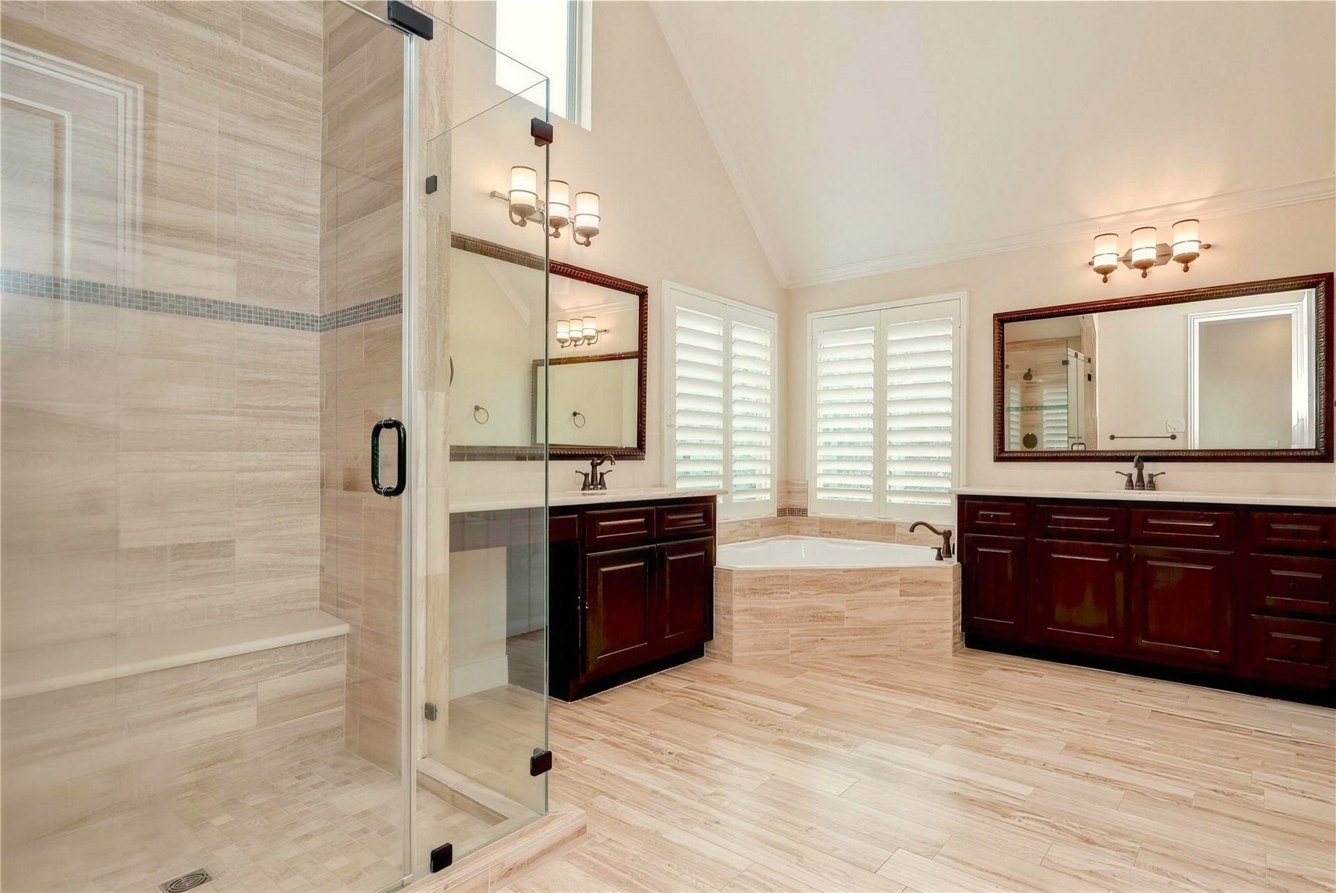 19 Herons Flight Place, Spring, TX 77389 Elegant bathroom featuring a spacious glass-enclosed shower, luxurious soaking tub, dual vanities with rich wood cabinetry, and abundant natural light through plantation shutters.