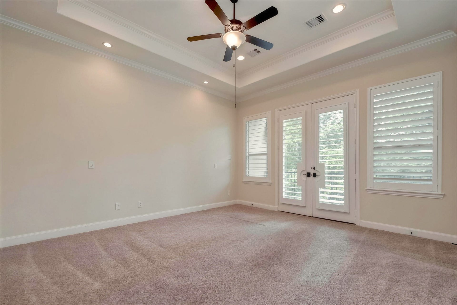 19 Herons Flight Place, Spring, TX 77389 Spacious bedroom with a tray ceiling, elegant fan, and ample natural light streaming through French doors and large windows with shutters.