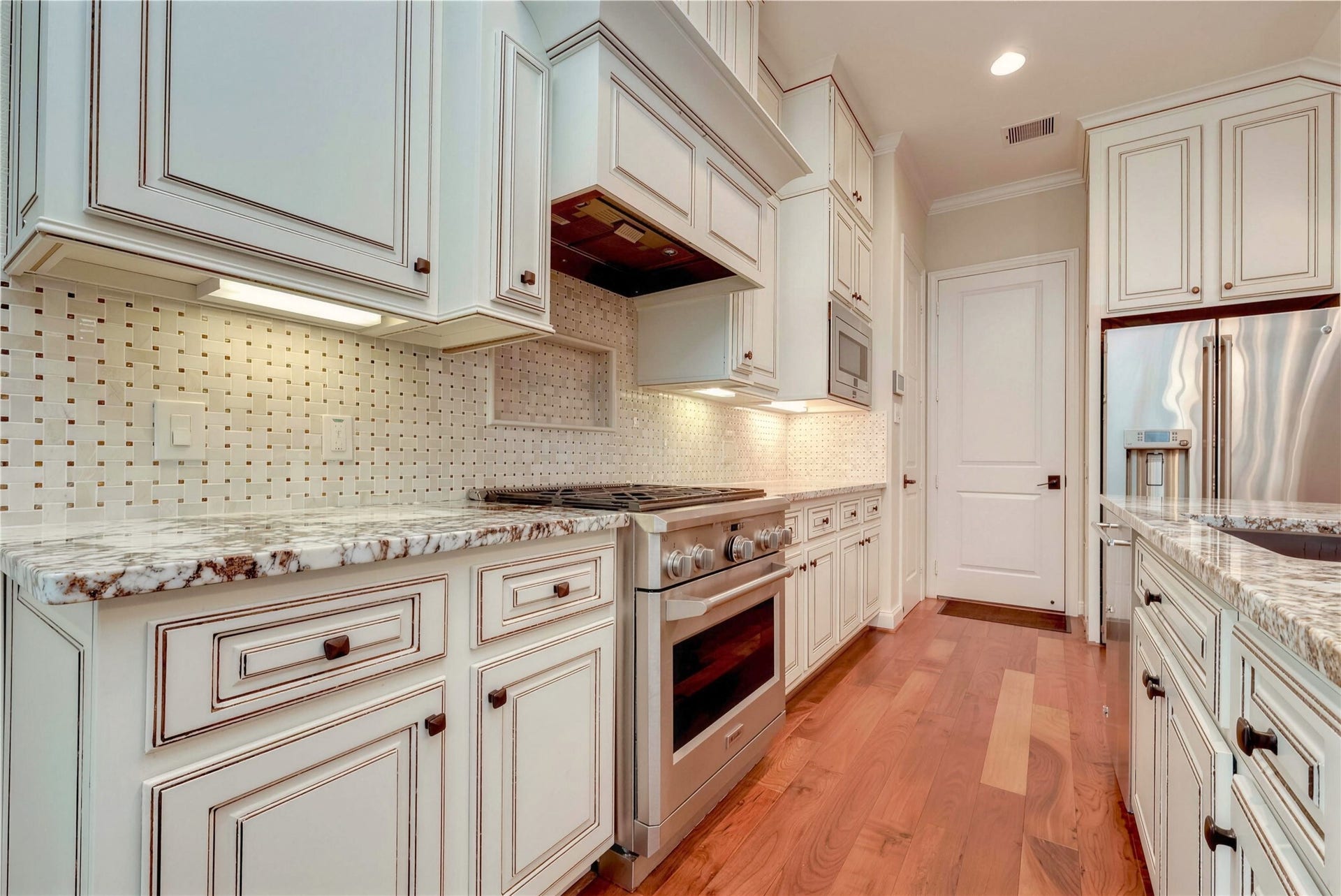 19 Herons Flight Place, Spring, TX 77389 Elegant kitchen with custom cabinetry, granite countertops, and modern stainless steel appliances, complemented by a stylish backsplash and warm wood flooring.