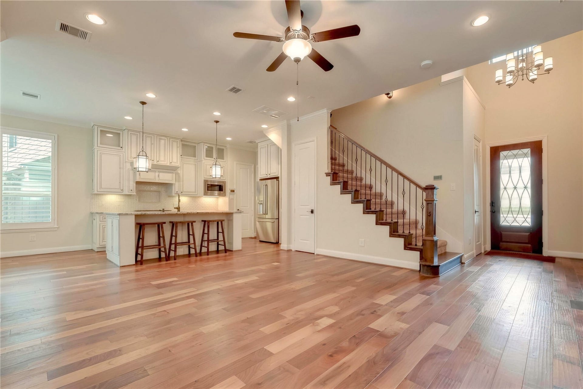 19 Herons Flight Place, Spring, TX 77389 Spacious open-concept living area with elegant hardwood floors, a modern kitchen featuring white cabinetry and stainless steel appliances, and a stylish staircase leading to the upper level.