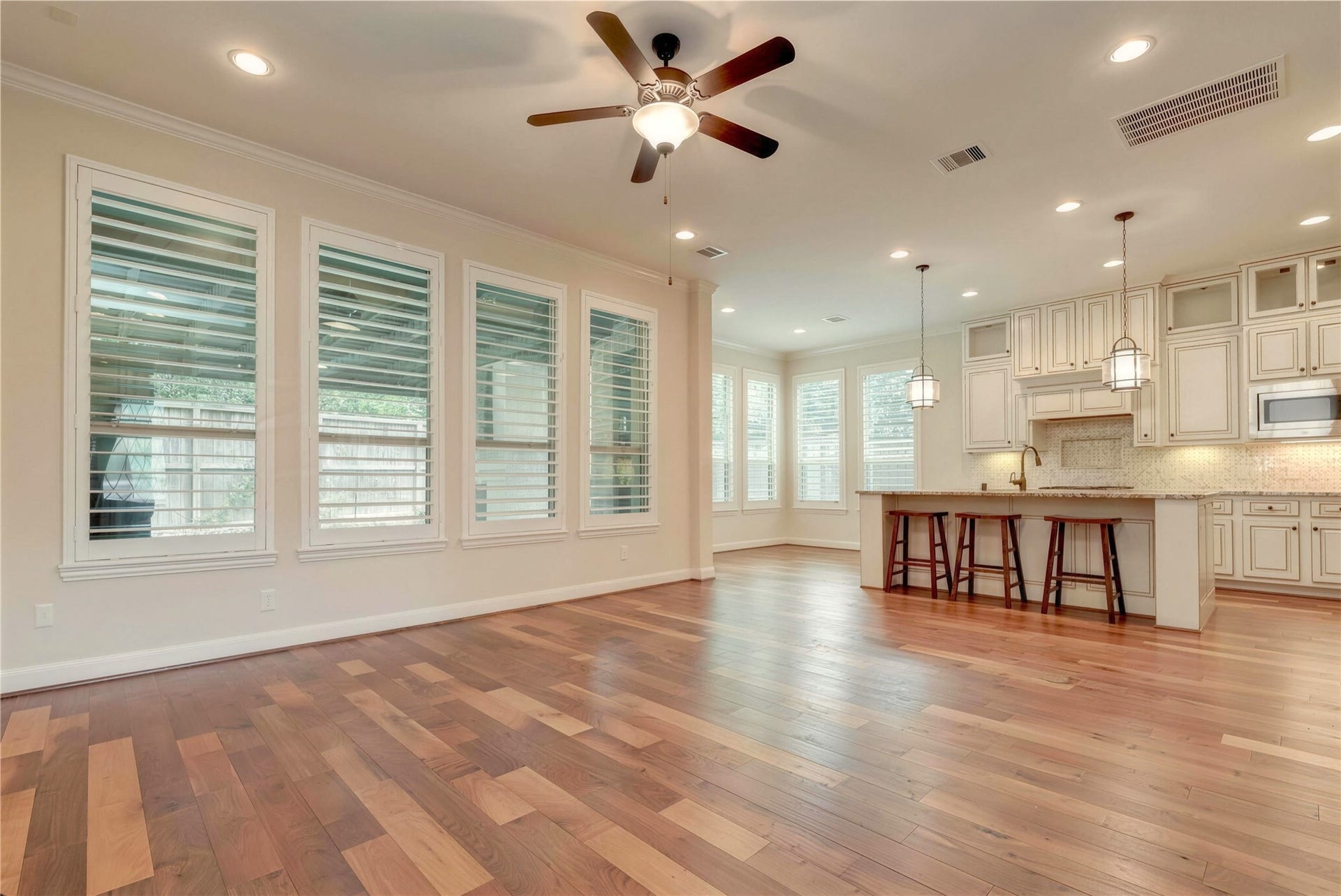 19 Herons Flight Place, Spring, TX 77389 Spacious open-plan living area with rich hardwood floors, abundant natural light from large windows, and a modern kitchen featuring elegant cabinetry, a large island with seating, and stylish pendant lighting.