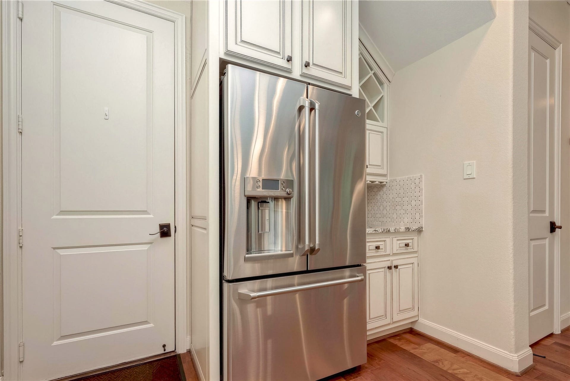 19 Herons Flight Place, Spring, TX 77389 Elegant kitchen corner featuring a sleek stainless steel refrigerator, complemented by white cabinetry and a stylish tile backsplash for a modern touch.