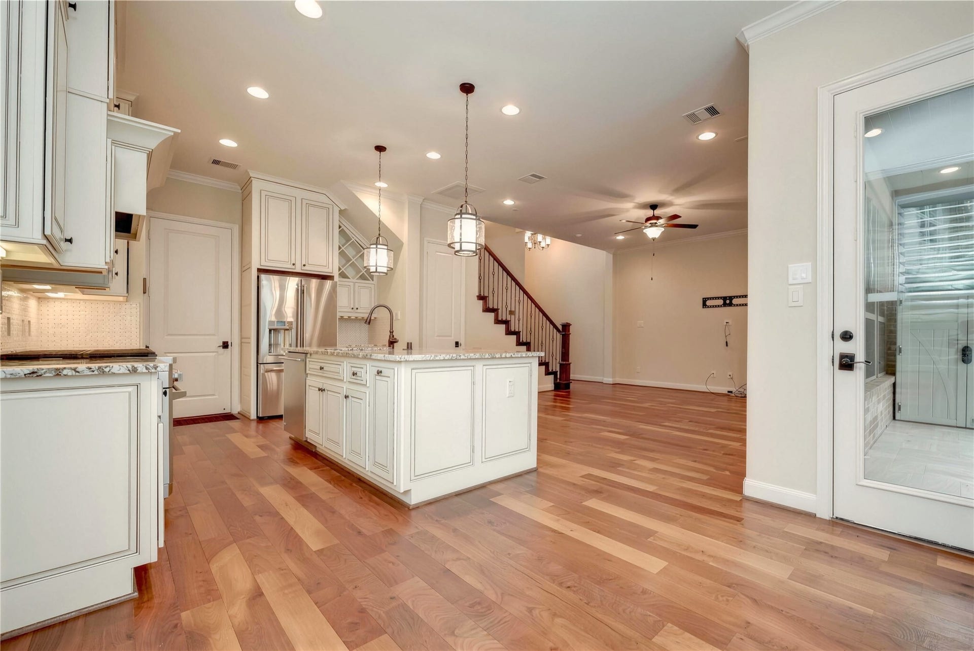 19 Herons Flight Place, Spring, TX 77389 Elegant open-concept kitchen and living area featuring hardwood floors, a central island with pendant lighting, and stainless steel appliances.