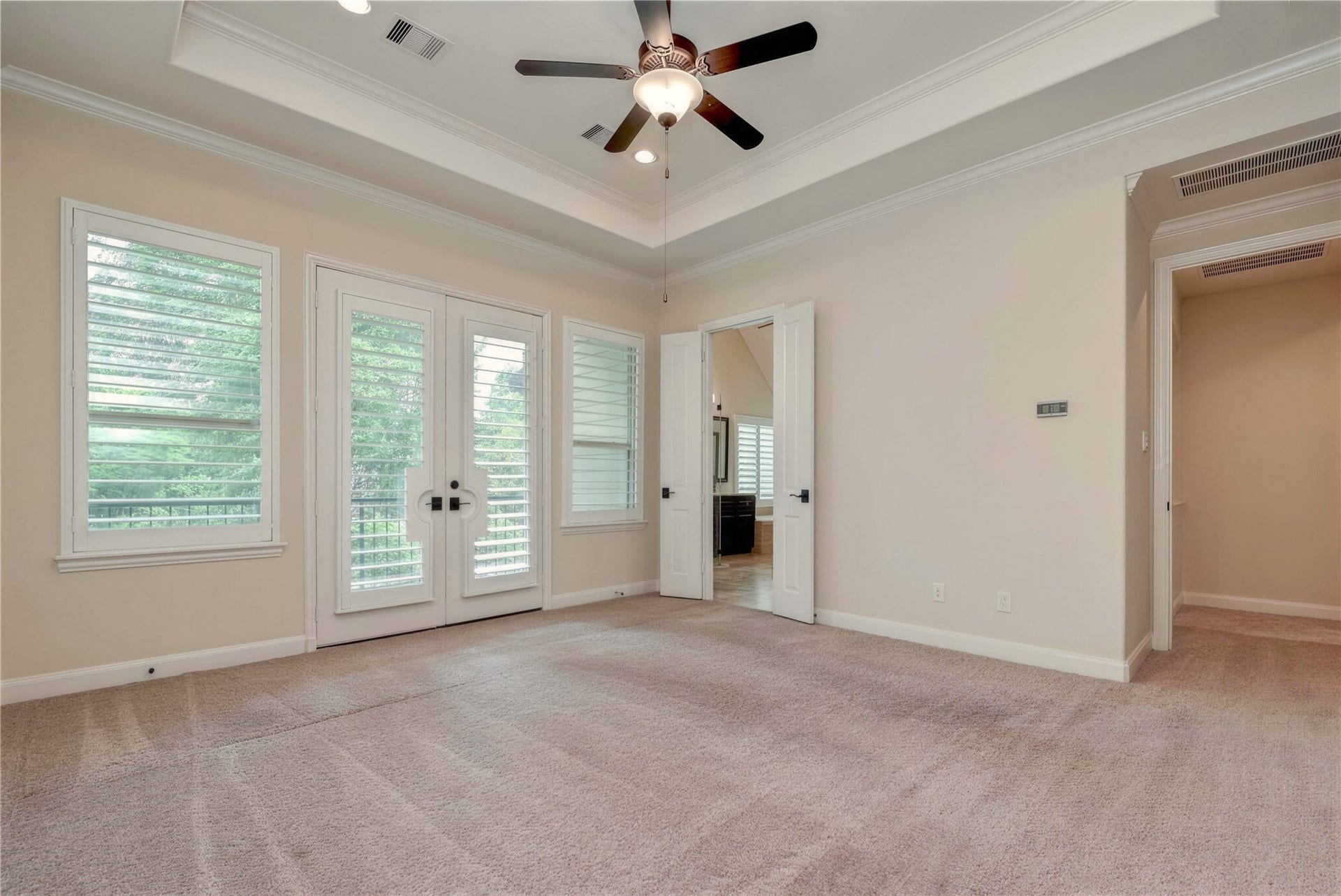 19 Herons Flight Place, Spring, TX 77389 Spacious bedroom with a tray ceiling, elegant ceiling fan, and abundant natural light streaming through large windows and French doors, offering a serene view of the outdoors.