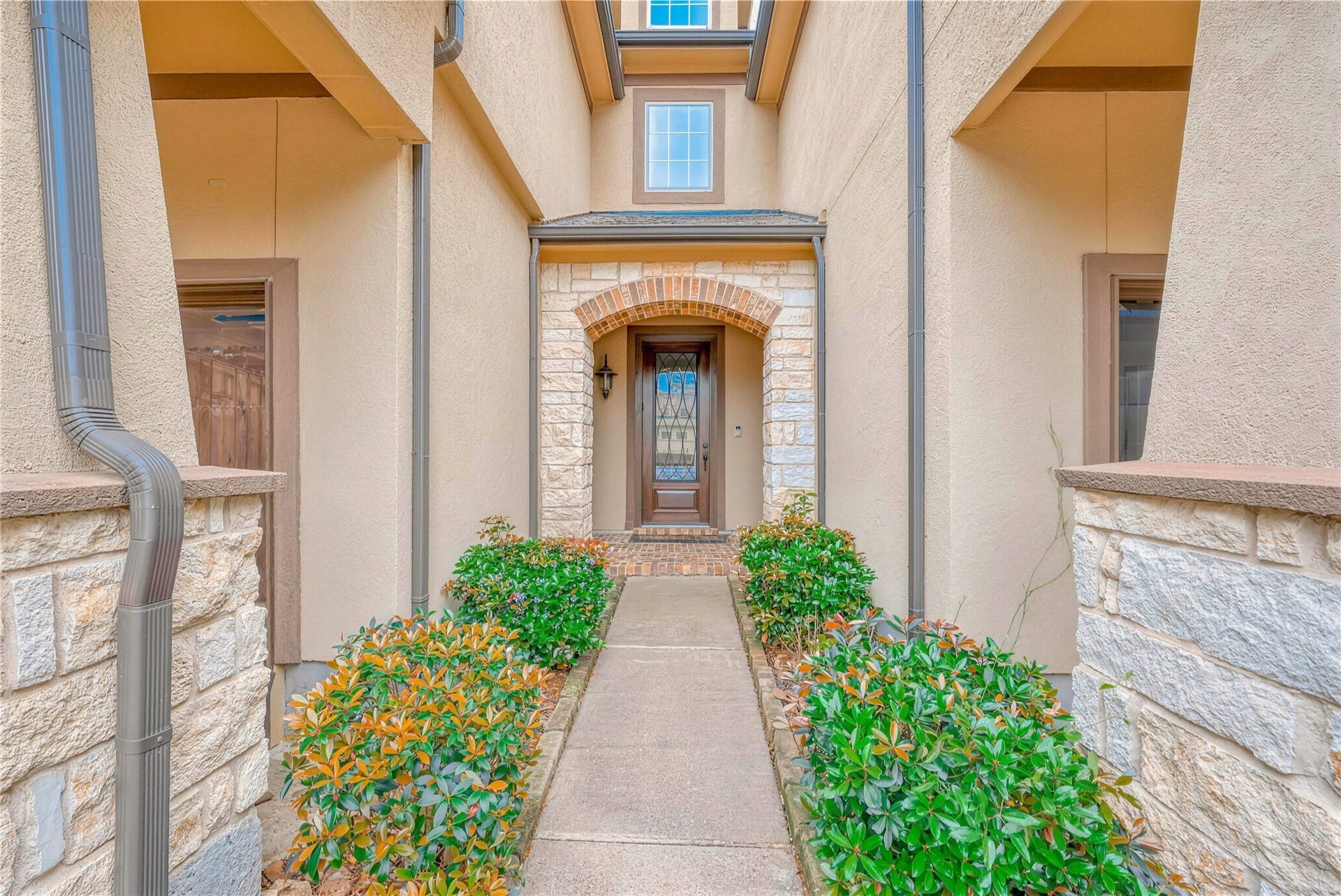 19 Herons Flight Place, Spring, TX 77389 Inviting entryway with a charming arched doorway, framed by elegant stonework and lush greenery, leading to a welcoming front door.