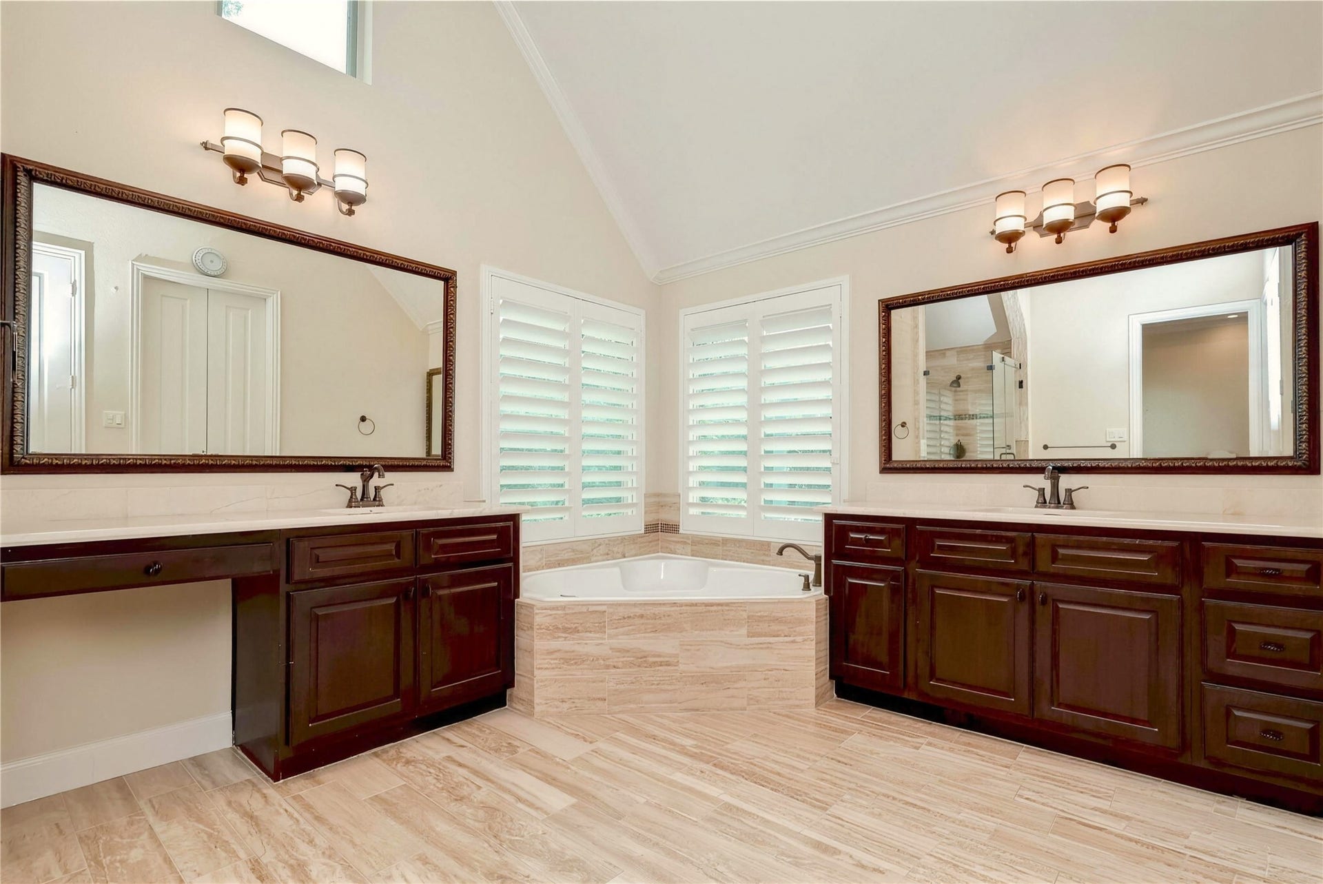 19 Herons Flight Place, Spring, TX 77389 Luxurious bathroom featuring dual vanities with elegant dark wood cabinetry, a spacious corner bathtub, and stylish lighting, all accented by large mirrors and natural light from shuttered windows.