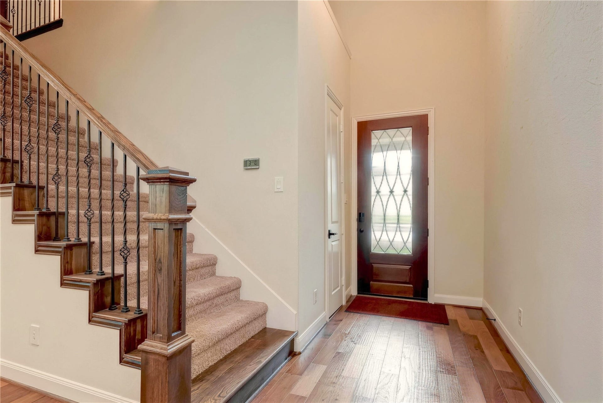 19 Herons Flight Place, Spring, TX 77389 Inviting entryway featuring a stylish wooden staircase with wrought iron balusters and a decorative front door with glass insets, complemented by warm hardwood flooring.