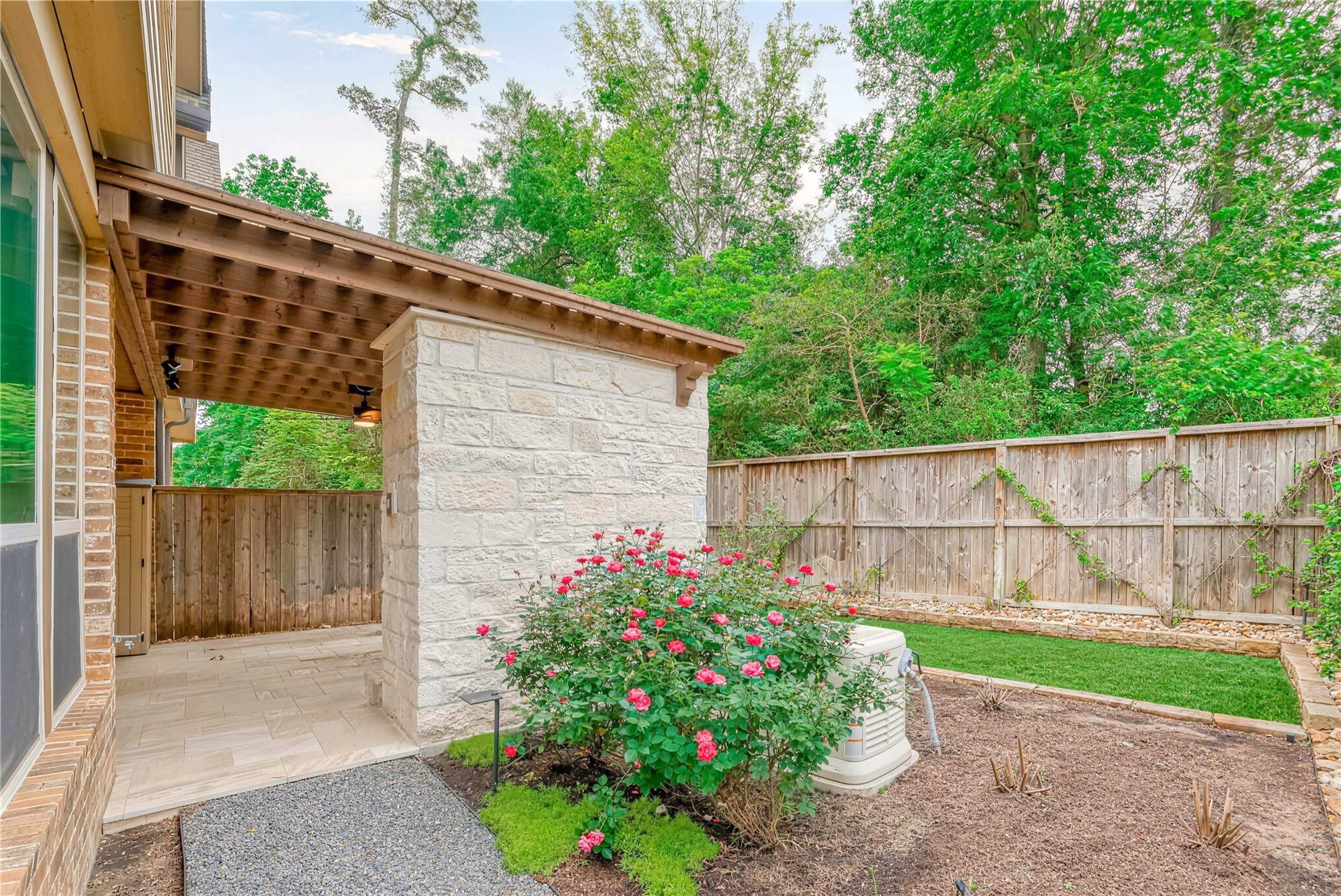 19 Herons Flight Place, Spring, TX 77389 Charming outdoor space featuring a covered patio with elegant stonework, a lush garden with blooming roses, and a private fenced yard surrounded by mature trees.