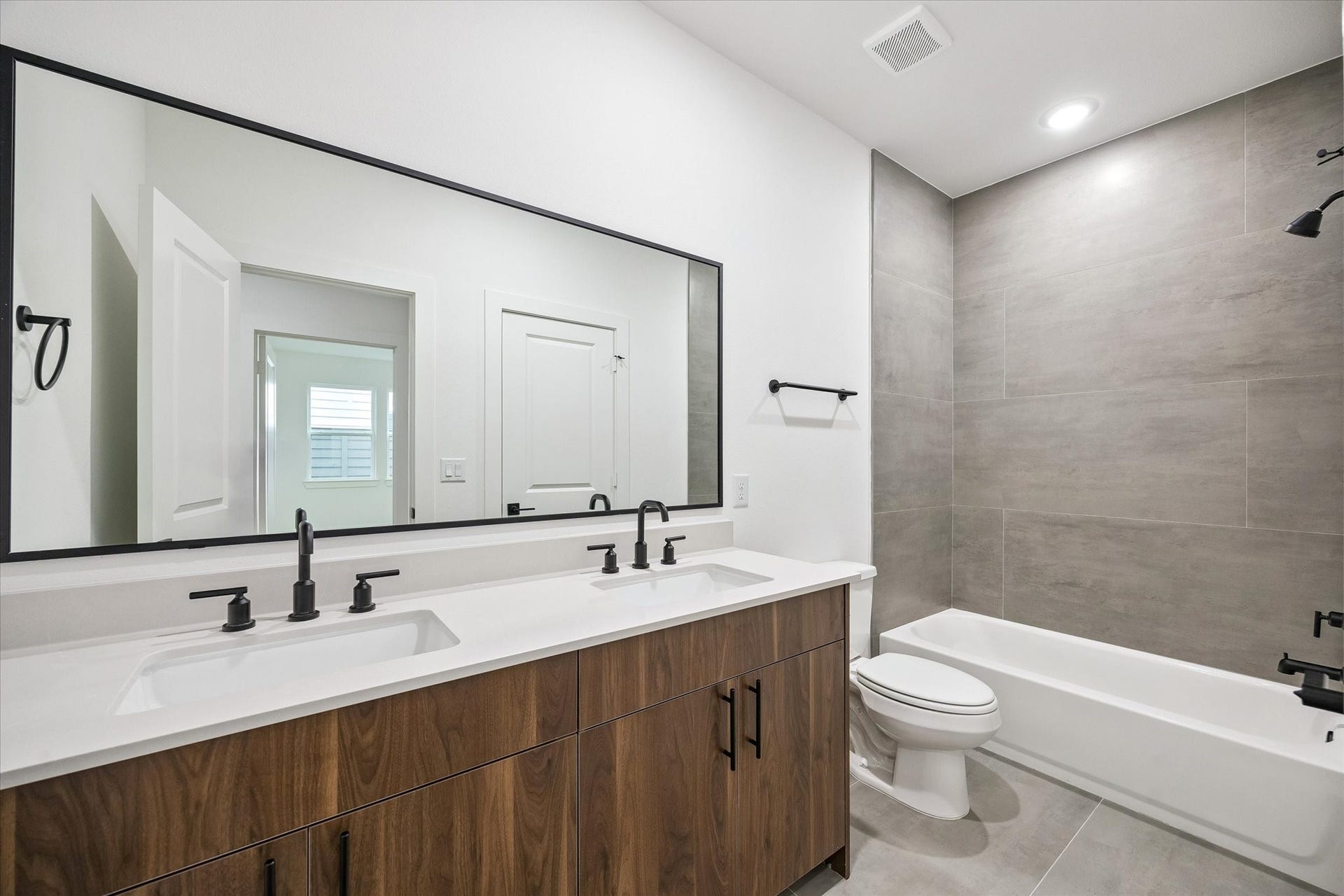 Full bath with dual vanity, large mirror, and sleek tile surround