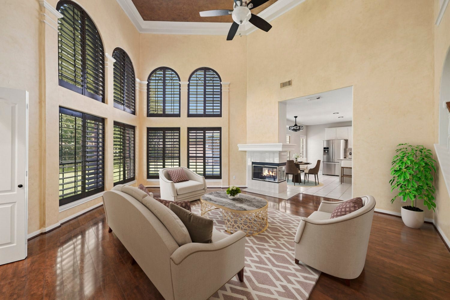 16 Fosters Court, Sugar Land, TX 77479 Virtually Staged: This impressive family room features soaring ceilings, rich wood flooring, and dramatic two-story arched windows that fill the space with natural light. A striking double-sided fireplace creates a warm focal point while connecting the family room to the adjoining living area. The spacious, open layout offers plenty of room for comfortable seating and entertaining.