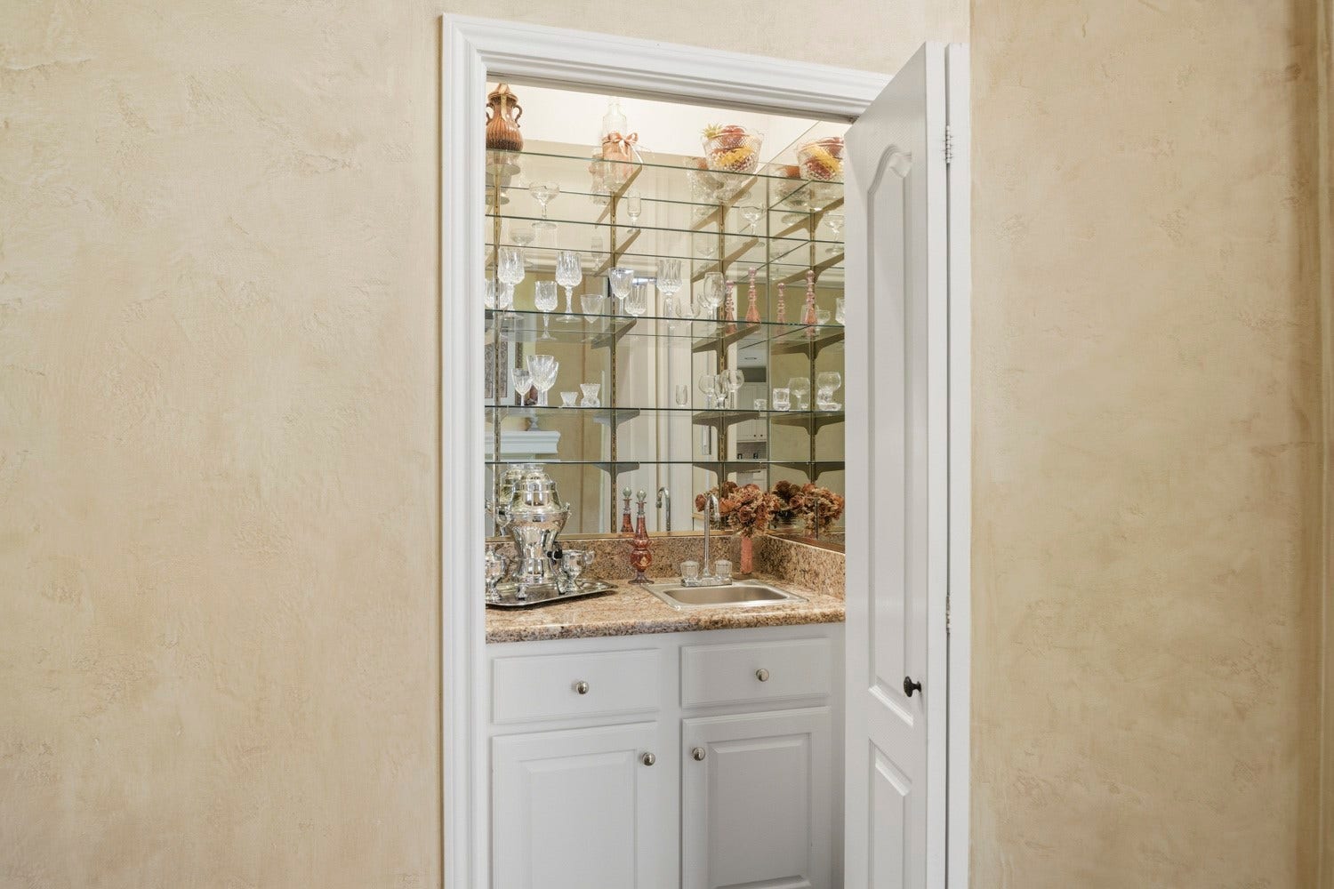 16 Fosters Court, Sugar Land, TX 77479 This built-in wet bar features mirrored walls, glass shelving, and a granite countertop with a small sink.