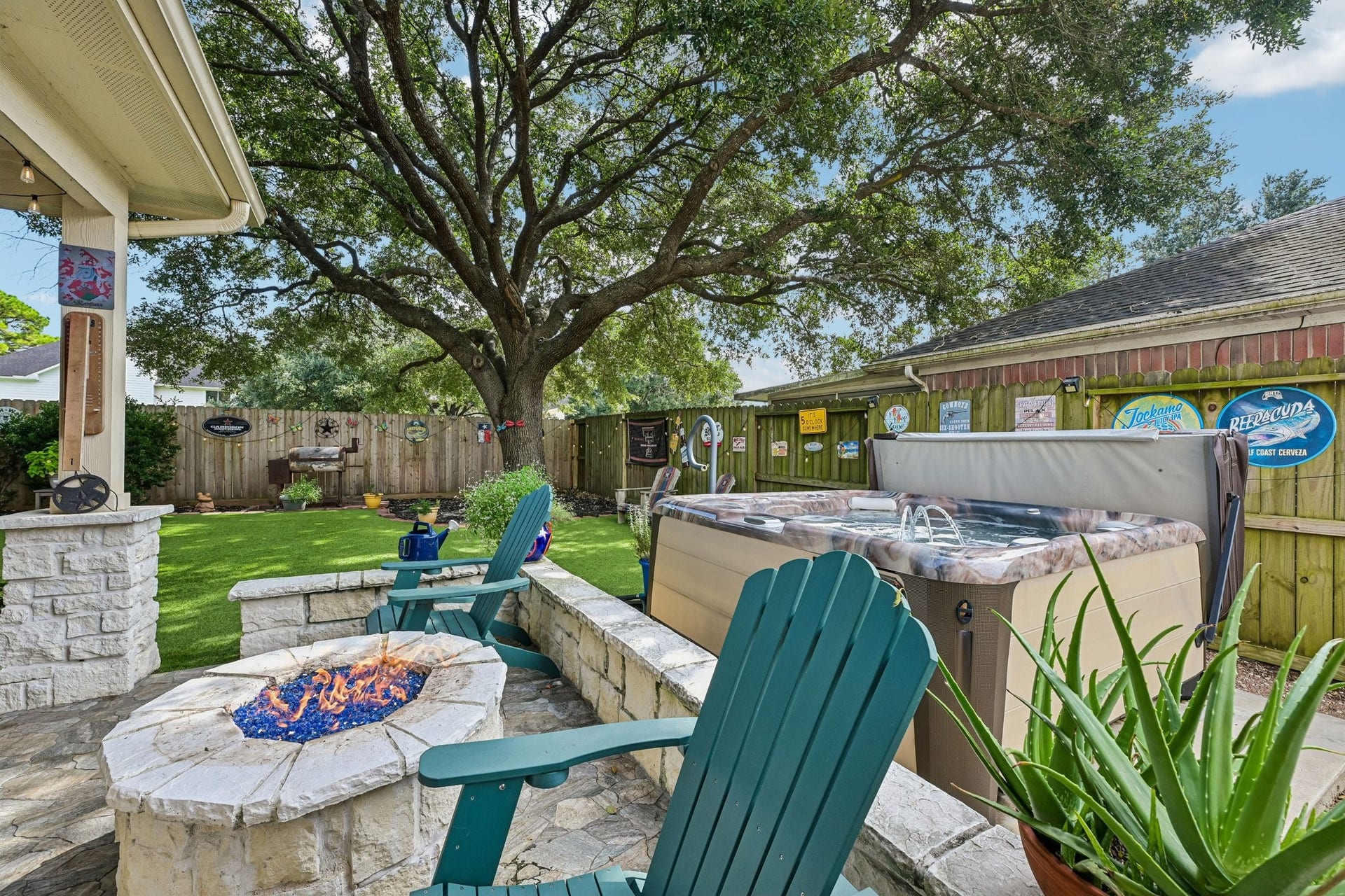14219 Cypress Ridge Drive, Cypress, TX 77429 Stone-built outdoor fire pit area with blue glass fire media and Adirondack seating positioned right next to the hot tub.