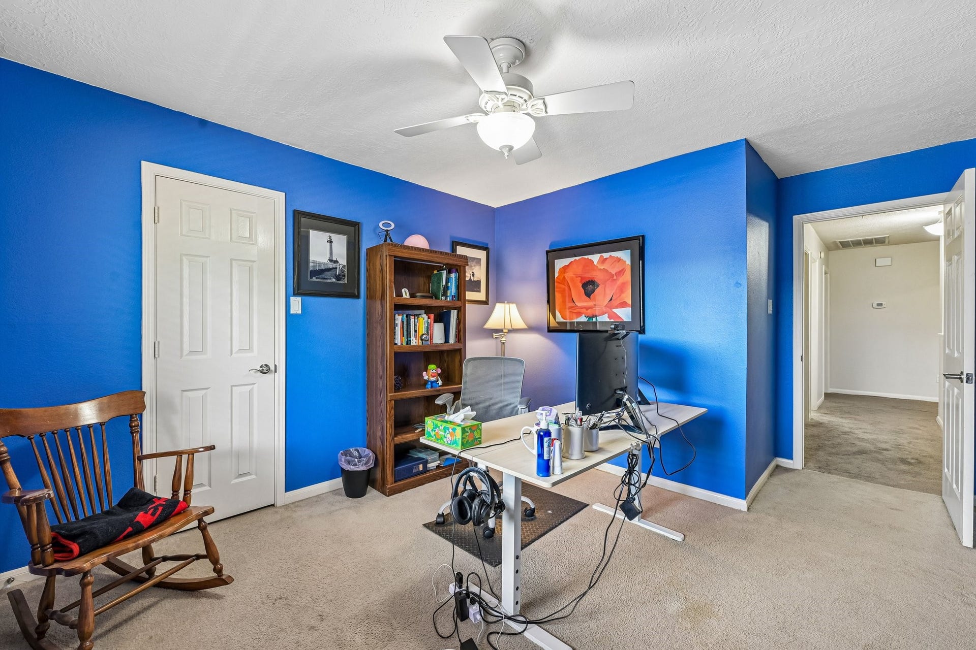 14219 Cypress Ridge Drive, Cypress, TX 77429 Spacious secondary bedroom/home office featuring vibrant blue accent walls, soft neutral carpeting, a ceiling fan, and direct hallway access.