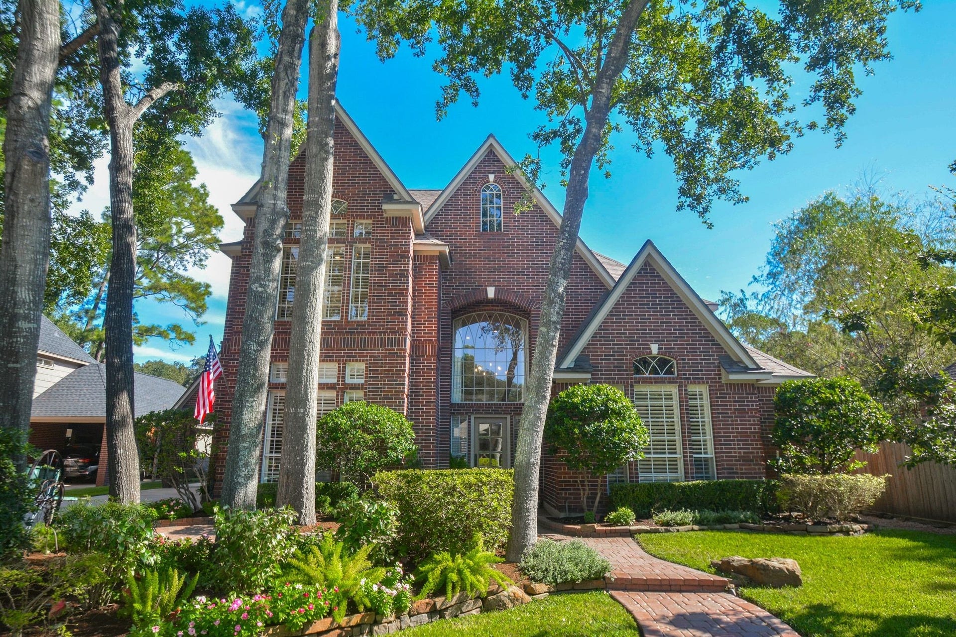 A winding brick walkway leads to the impressive arched entry, framed by mature shade trees, manicured landscaping, and distinctive brick architecture.