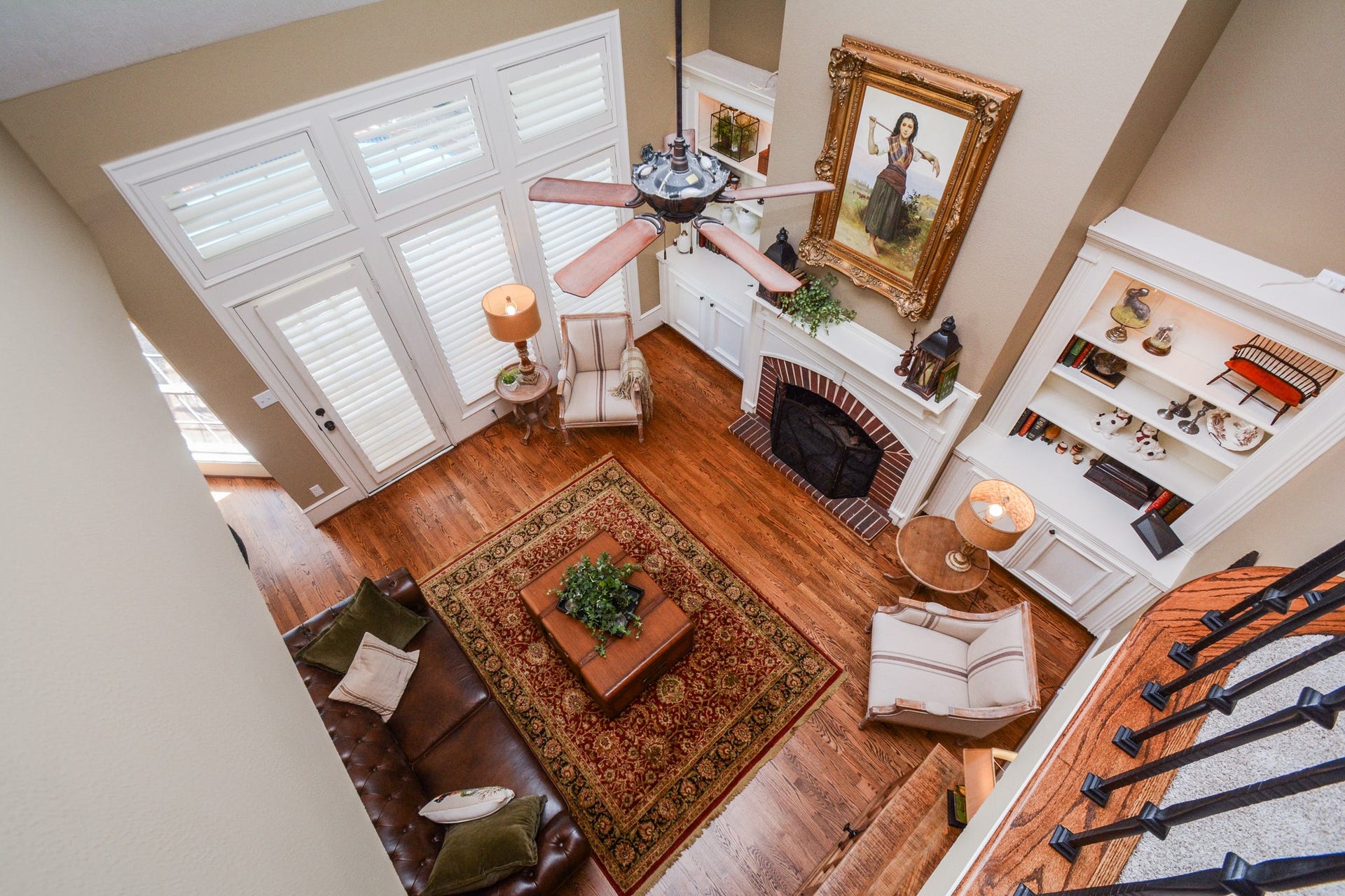 The upstairs overlook showcases the family rooms soaring ceiling, tall windows, fireplace, and beautiful hardwood flooring below.