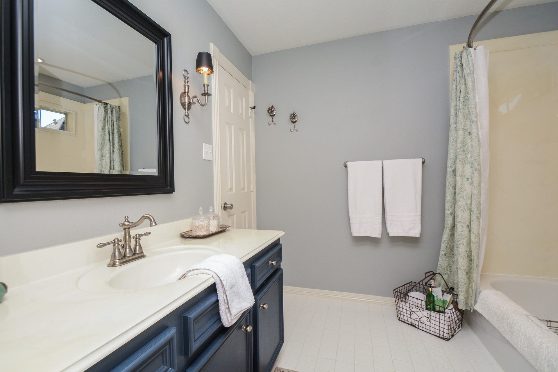 Blue vanity cabinetry, a framed mirror, and a tub-and-shower combination give this secondary upstairs bathroom a classic look.