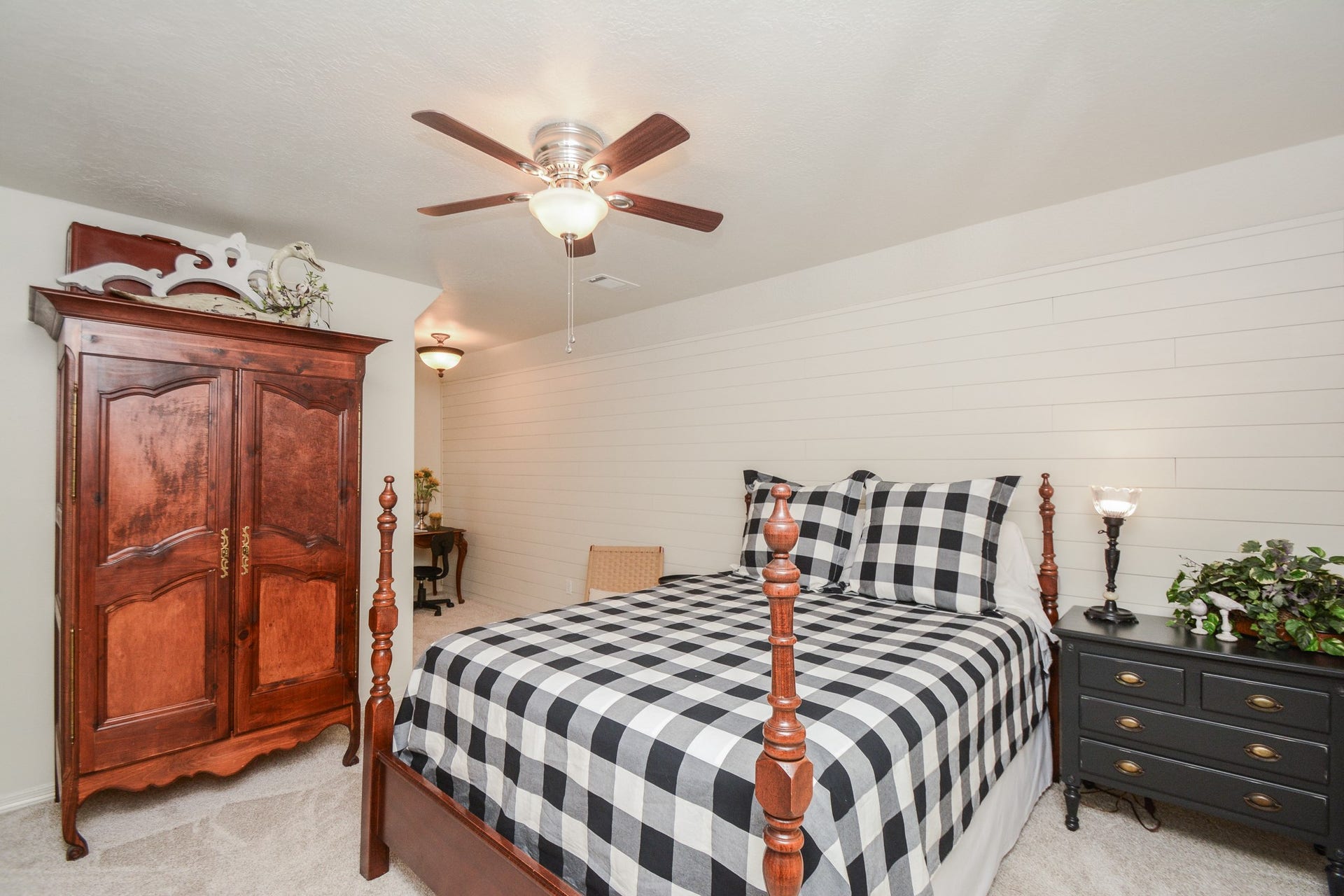 This upstairs secondary bedroom features a white plank accent wall, a ceiling fan, and a secluded area for reading or study.