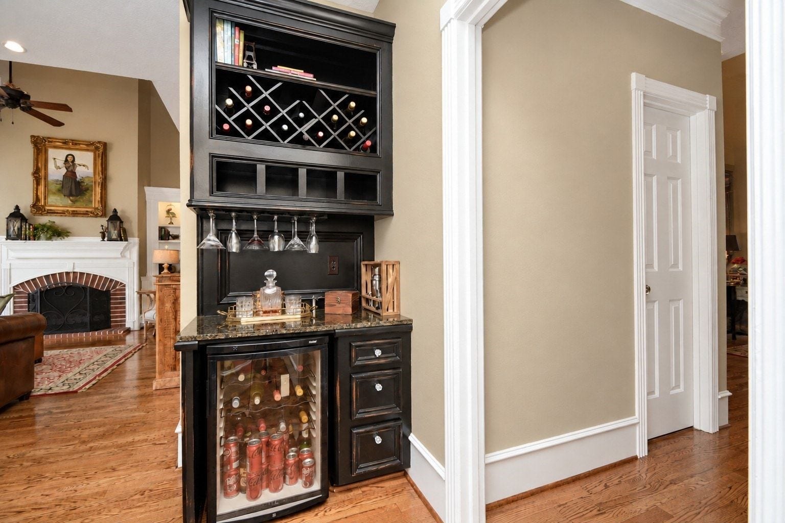 A built-in beverage station features wine storage, hanging stemware racks, a granite countertop, and a glass-front beverage refrigerator.
