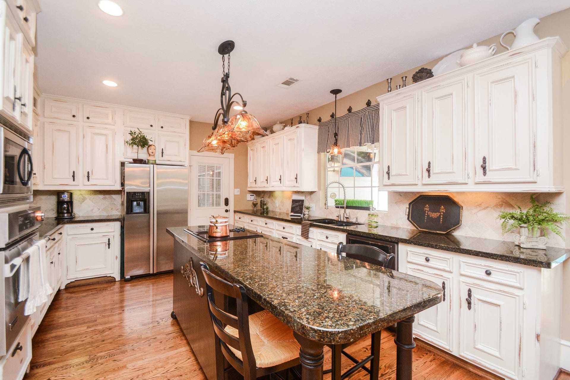The well-appointed kitchen features white cabinetry, granite countertops, hardwood flooring, and a spacious island with seating.