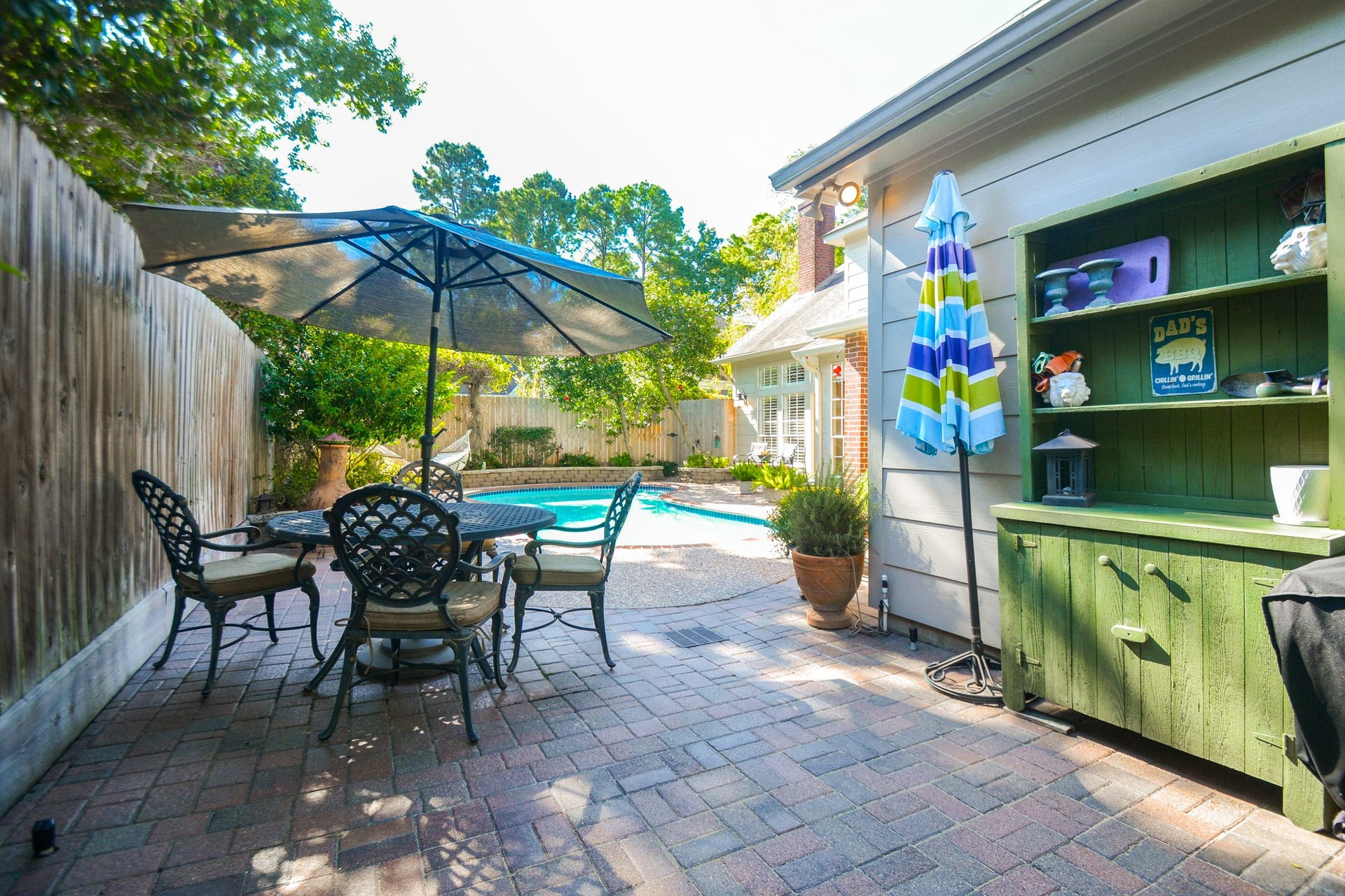 A brick-paved side patio with a colorful outdoor serving station offers a convenient gathering spot beside the pool.