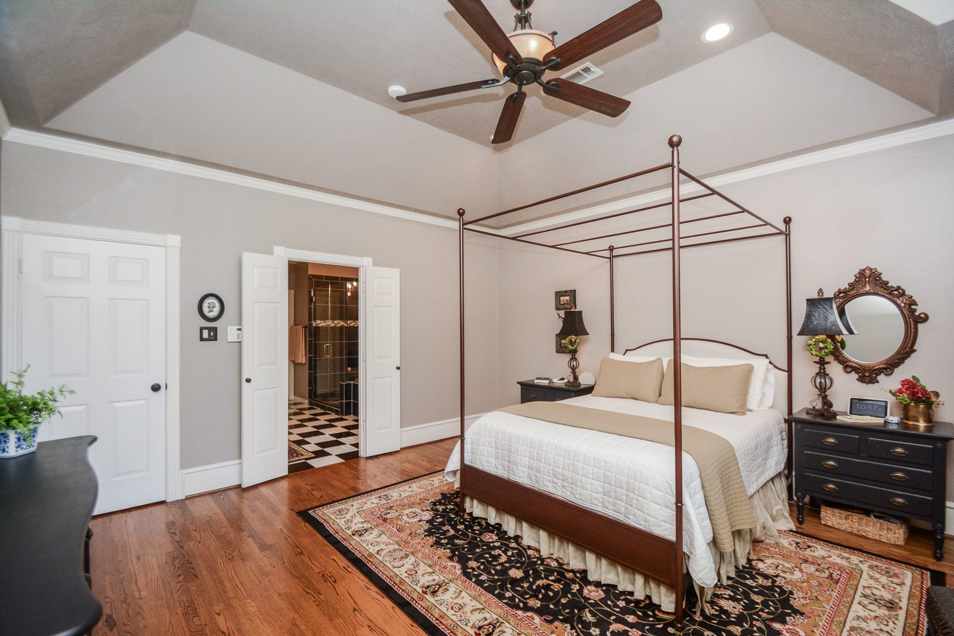 This alternate view showcases the primary bedrooms tray ceiling, hardwood flooring, and direct access to the adjoining private ensuite bathroom.