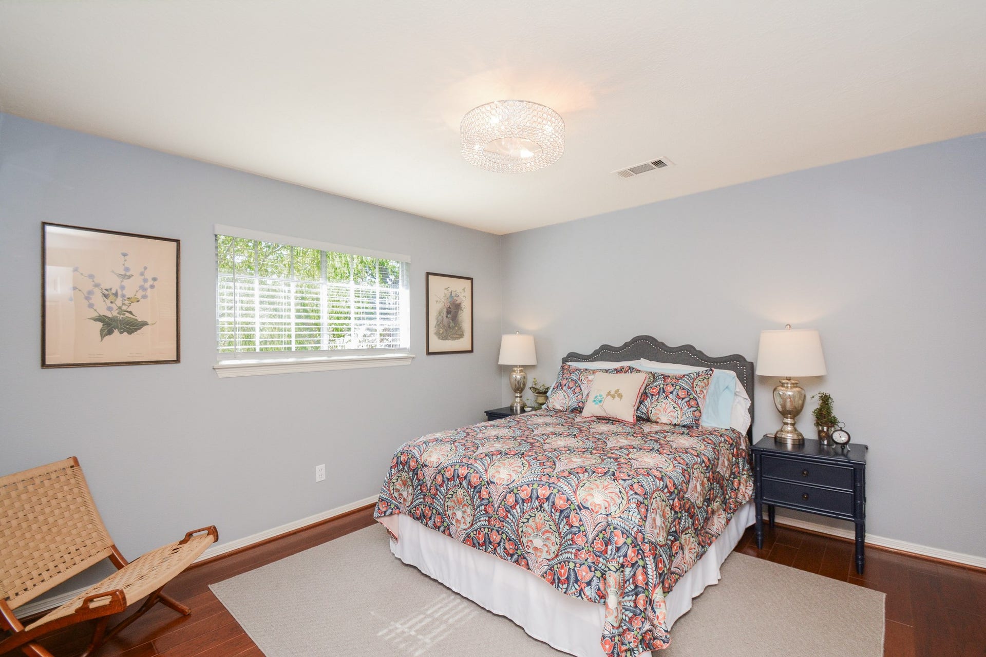 Soft blue walls, a wide window that welcomes natural light, and warm wood flooring create an inviting retreat in this upstairs secondary bedroom.