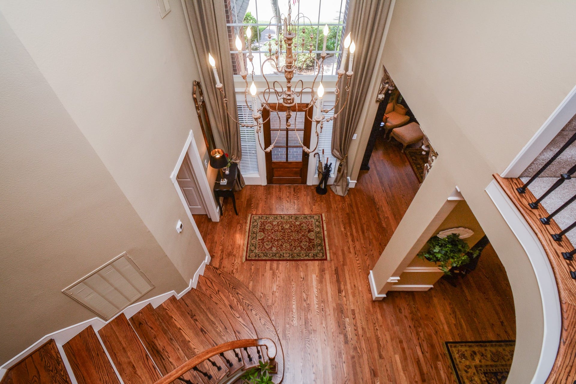 This view from upstairs highlights the dramatic foyer, curved staircase, decorative iron balusters, and hardwood floors.