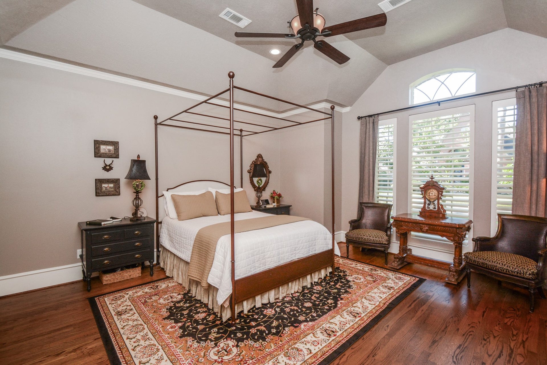 The downstairs primary bedroom offers beautiful hardwood flooring, a tray ceiling, and tall windows overlooking the greenery outside.