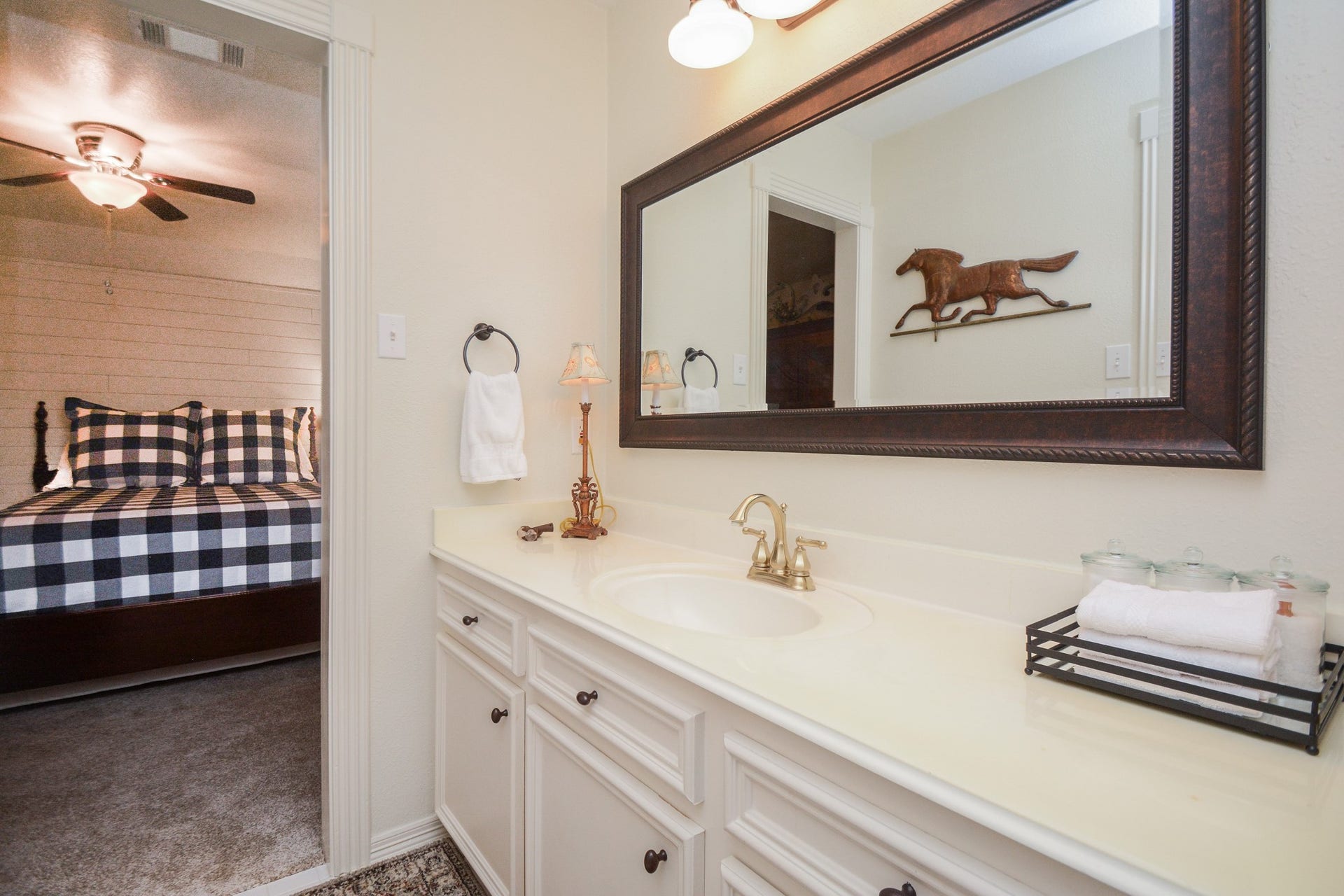 A spacious vanity with white cabinetry and a large framed mirror provides a convenient dressing area beside the secondary ensuite bedroom.