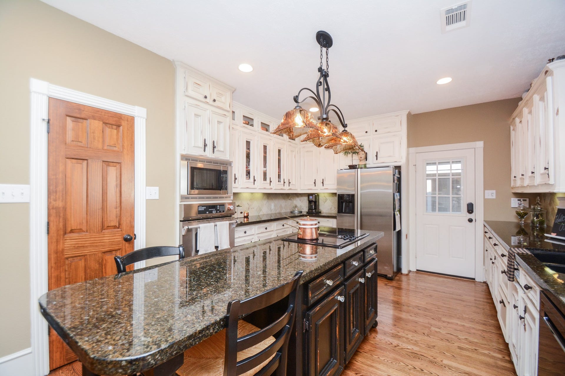 Pendant lighting illuminates the granite-topped island, complemented by stainless steel appliances and beautiful hardwood floors.