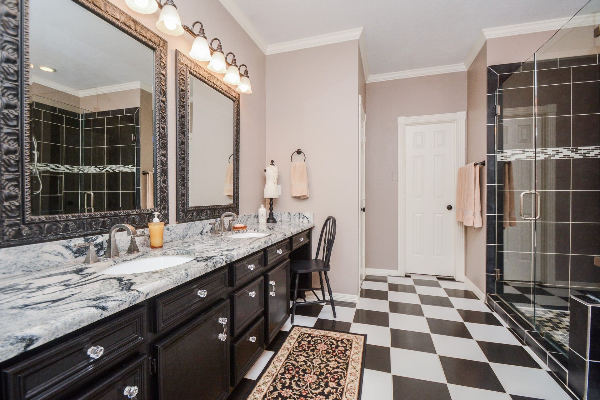 The primary bathroom features an expansive double-sink vanity, framed mirrors, and striking black-and-white finishes.