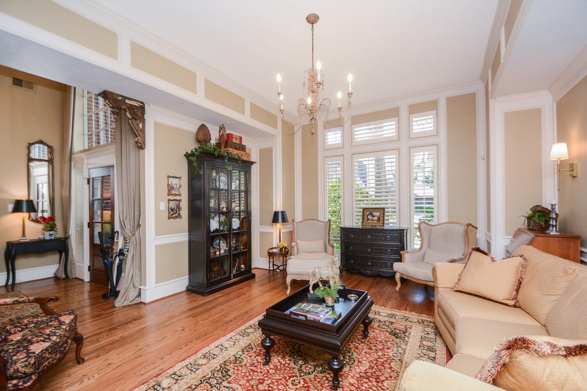 A chandelier, decorative ceiling details, and hardwood floors lend classic charm to the light-filled living room.