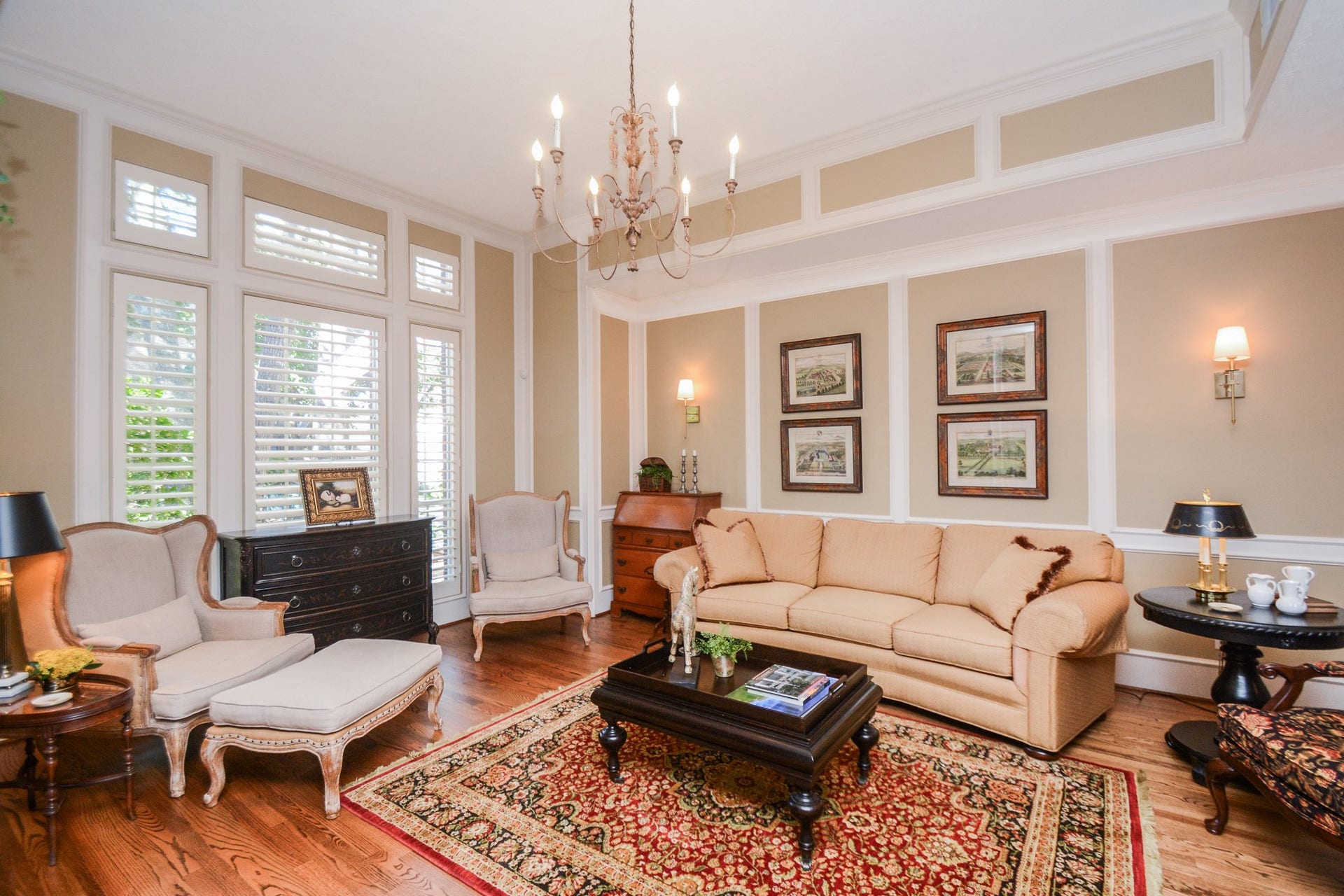 The elegant living room features hardwood floors, detailed crown molding, and tall windows with plantation shutters.