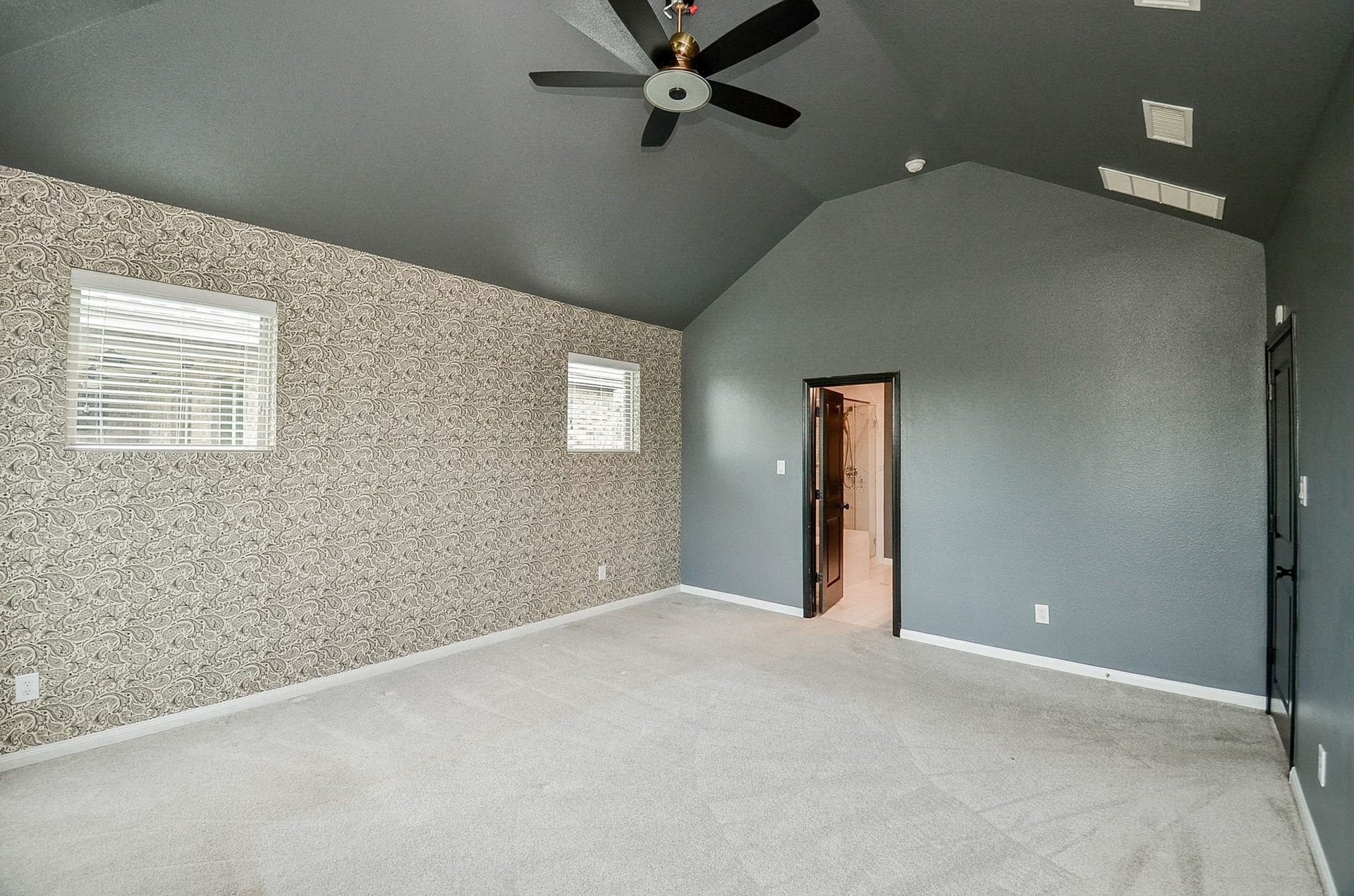 860 Marisol Bay Drive, Katy, TX 77493 The primary bedroom is on the main floor and features a vaulted ceiling, elegant accent wallpaper, and natural light from dual windows. A ceiling fan adds comfort, and an attached en-suite offers convenience.