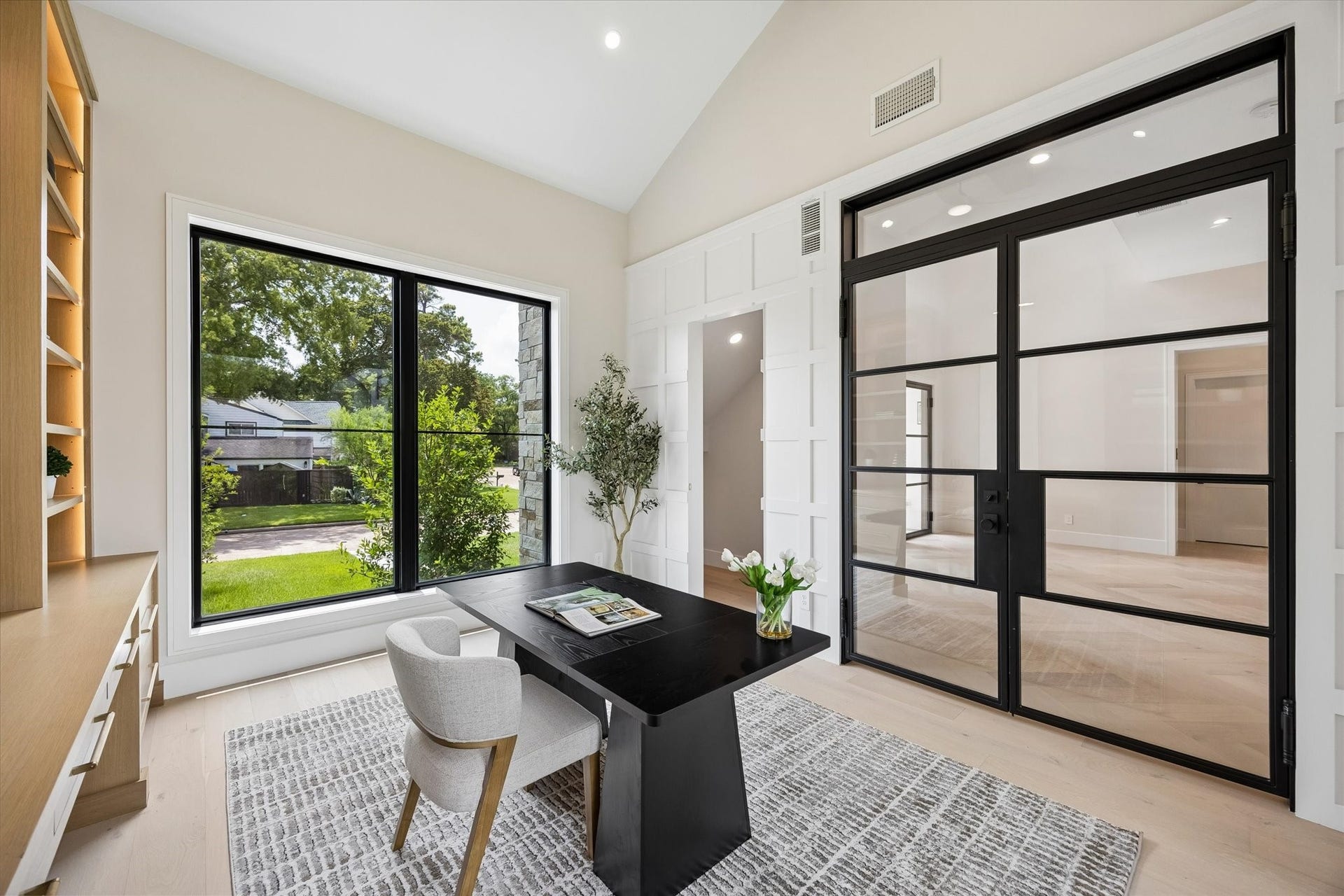 14106 Heatherfield Drive, Houston, TX 77079 A light-filled home office makes an unforgettable first impression with soaring ceilings, dramatic black-framed glass doors and an oversized picture window framing lush front-yard views. Custom built-in cabinetry and illuminated shelving bring warmth and function, while wide-plank flooring and crisp architectural millwork add a refined finish. With abundant natural light and a polished, private setting, this sophisticated workspace is designed to make working from home feel effortless.