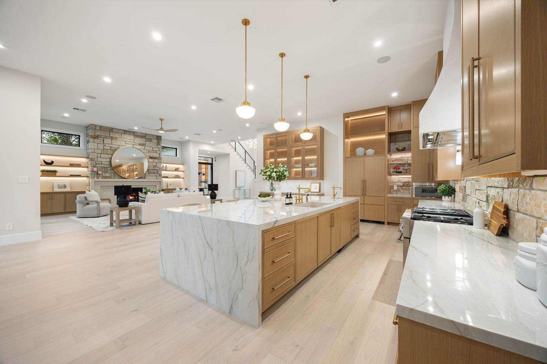 14106 Heatherfield Drive, Houston, TX 77079 A stunning open-concept kitchen and living space designed for both everyday living and effortless entertaining. The oversized waterfall island anchors the room with clean lines and elegant stone surfaces, complemented by warm wood cabinetry and soft ambient lighting. The true standout is the seamless connection to the living area, where a floor-to-ceiling stone fireplace creates a striking focal point, blending texture, warmth, and modern sophistication.