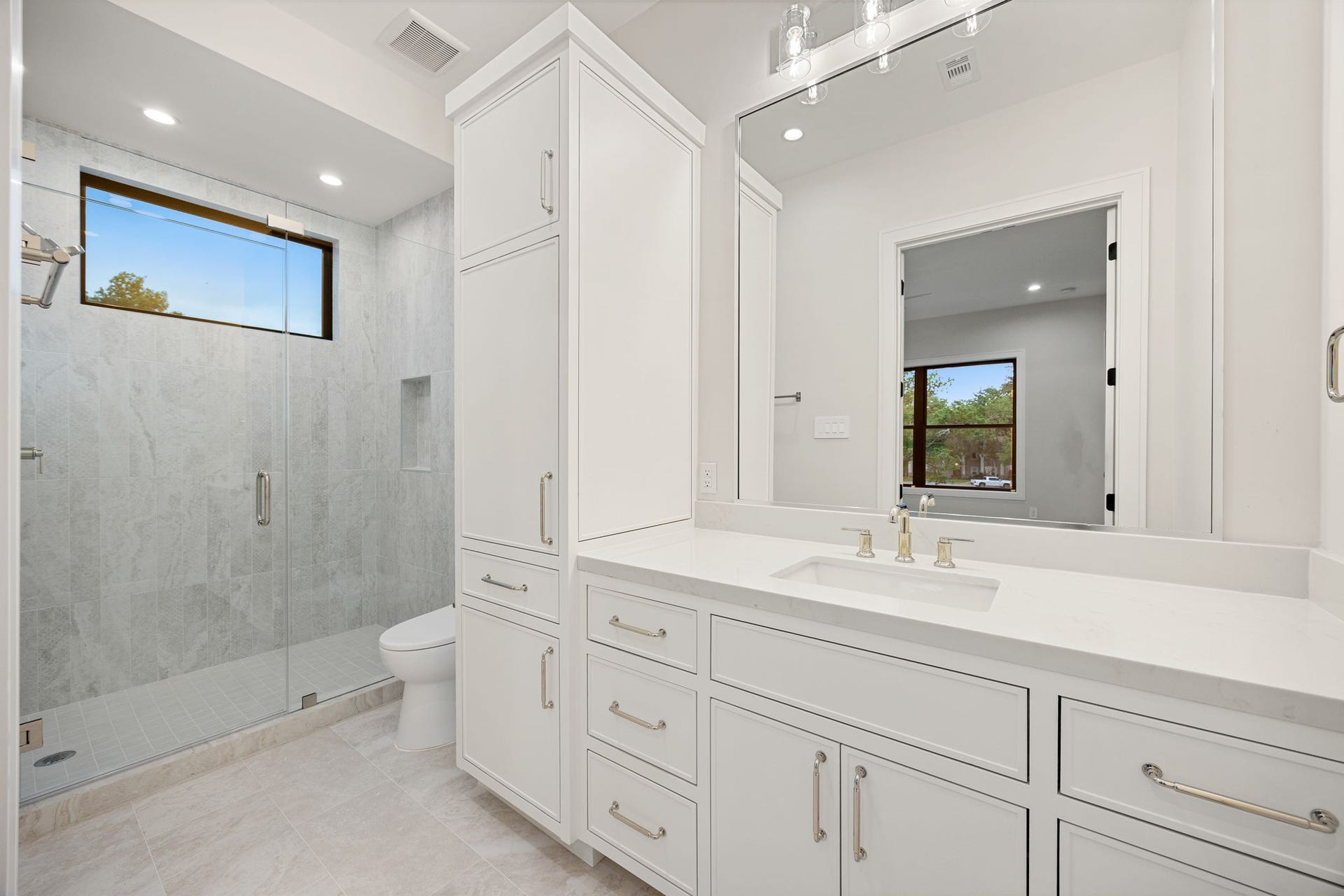 14106 Heatherfield Drive, Houston, TX 77079 A bright and elegant bathroom designed with timeless finishes and thoughtful functionality, featuring a spacious vanity, abundant cabinetry, and sleek hardware. Natural light filters in, enhancing the clean, airy feel throughout. The highlight of this space is the oversized glass-enclosed walk-in shower with floor-to-ceiling tile and a built-in niche, creating a spa-like retreat perfect for everyday relaxation and comfort.