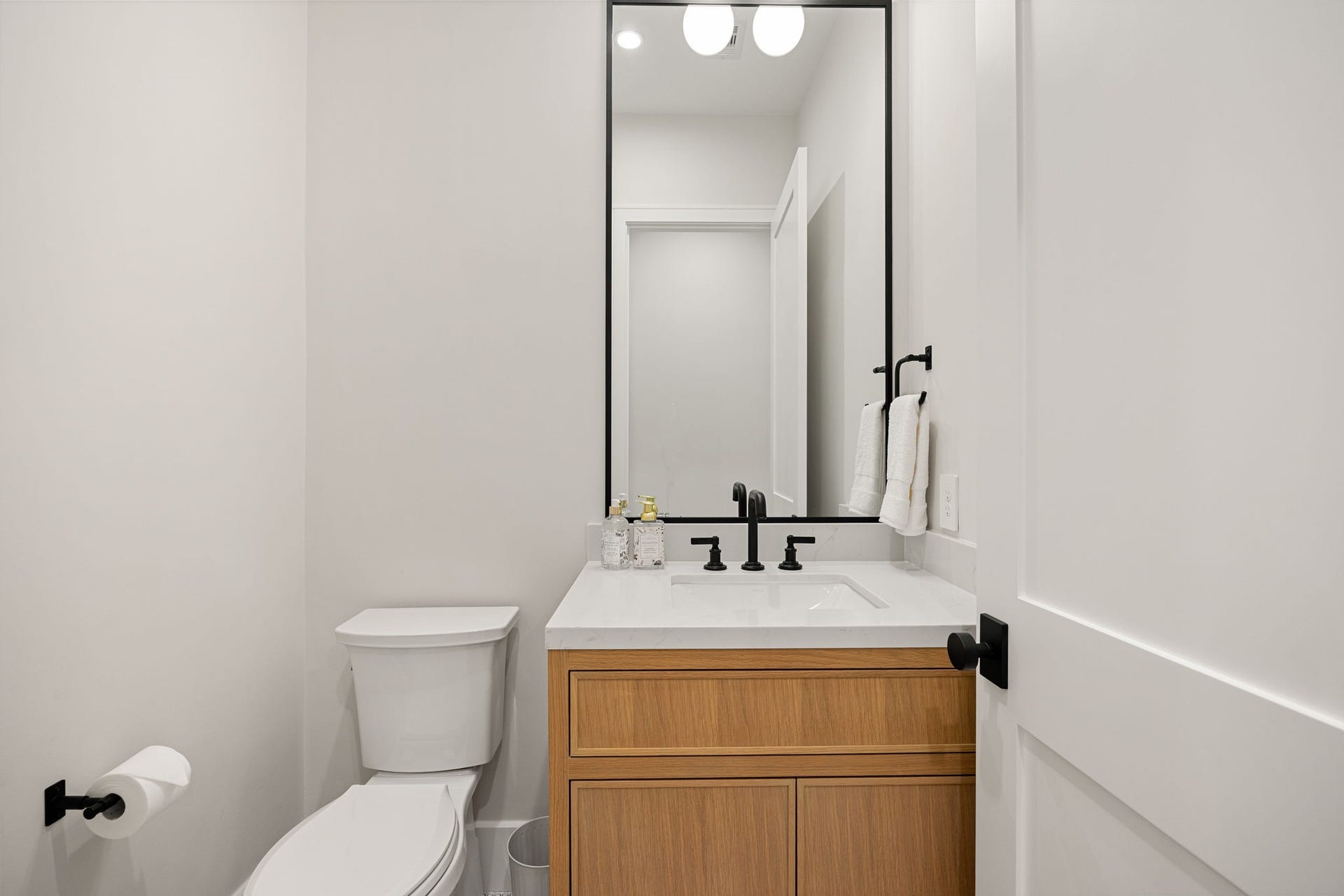 14106 Heatherfield Drive, Houston, TX 77079 A sleek and functional powder room designed with modern appeal, featuring warm wood cabinetry, a crisp white countertop, and matte black fixtures. Clean lines and minimal design create a sophisticated look. The highlight of this space is the striking contrast between the wood vanity and bold black hardware, adding depth and contemporary style to this compact yet impactful room.