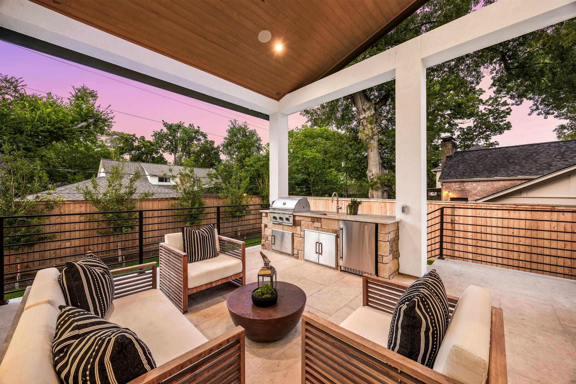 14106 Heatherfield Drive, Houston, TX 77079 A beautifully designed outdoor lounge area that offers both comfort and sophistication, with ample seating arranged for conversation and relaxation. Surrounded by mature trees and privacy fencing, it feels like a private retreat. The highlight of this space is the custom outdoor kitchen and grilling station, ideal for hosting gatherings and enjoying evenings under the open sky.