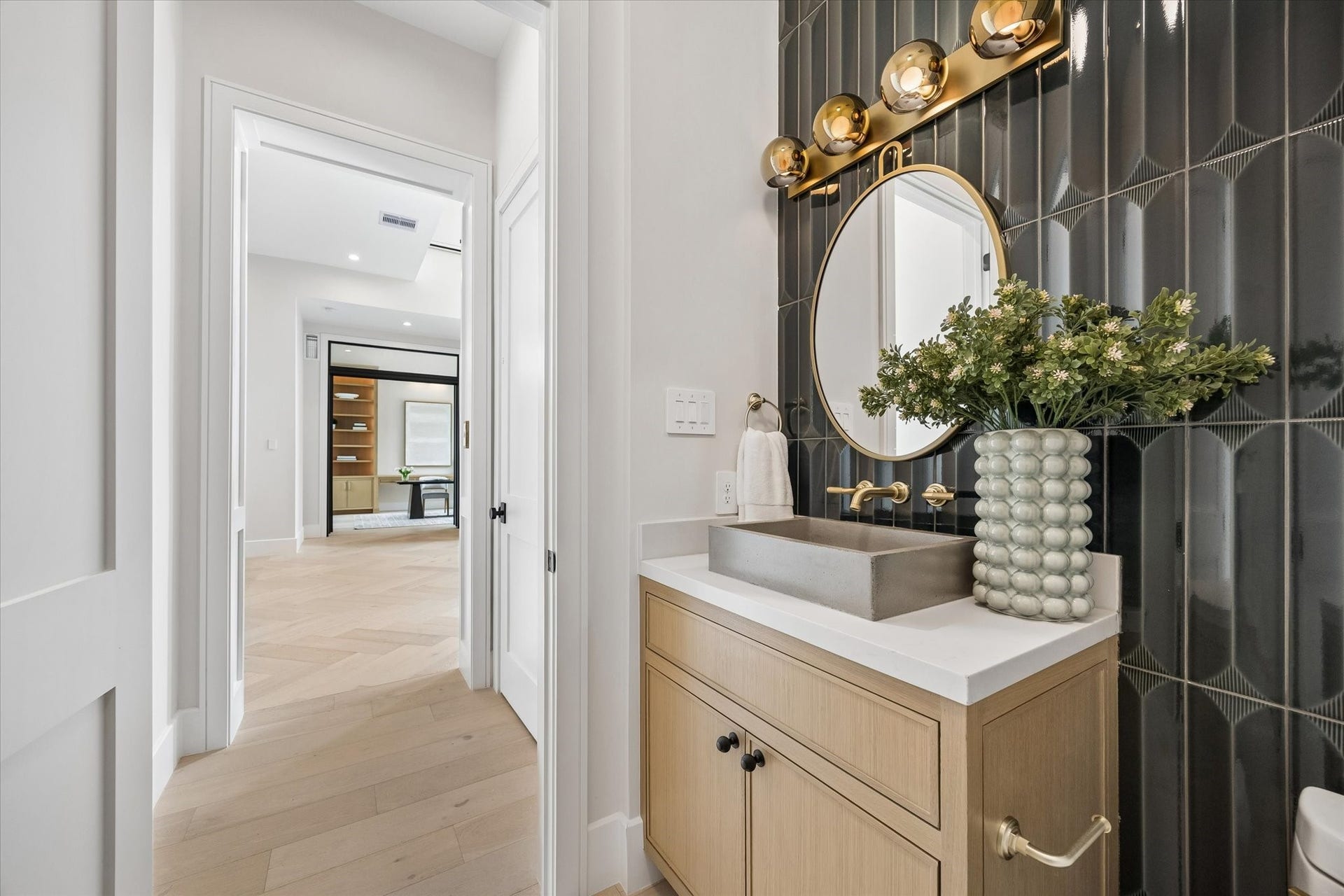 14106 Heatherfield Drive, Houston, TX 77079 This jewel-box powder room delivers memorable style through rich texture and sophisticated contrast. Glossy dark dimensional tile creates a dramatic feature wall behind a warm wood vanity, sculptural vessel sink and wall-mounted brass fixtures. A round brass-framed mirror and statement lighting complete the polished composition, balancing contemporary design with inviting natural materials for a guest space that feels both luxurious and distinctive.