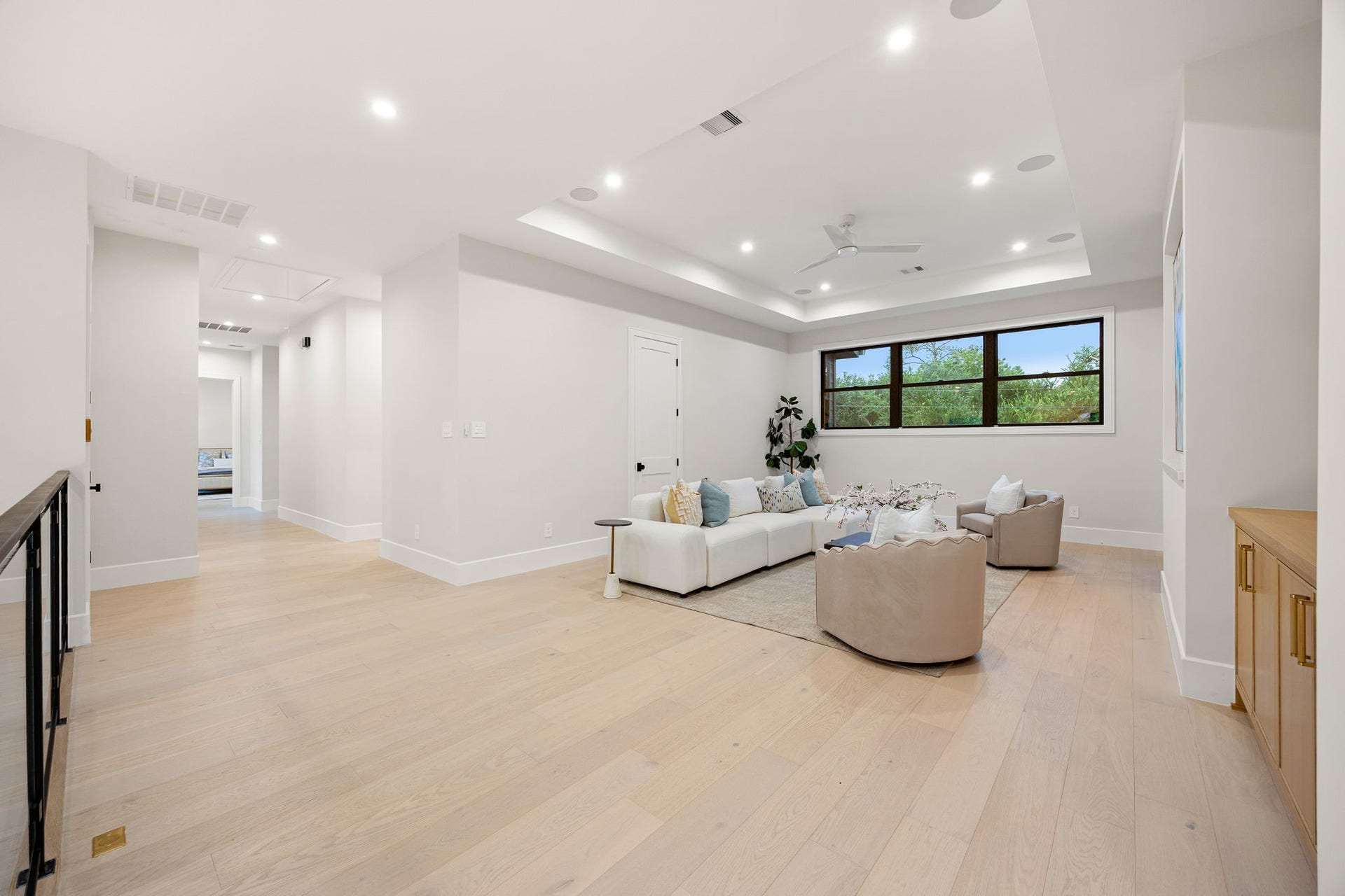 14106 Heatherfield Drive, Houston, TX 77079 This expansive living area offers a bright, open layout perfect for relaxing or entertaining, with wide-plank flooring and clean modern finishes throughout. Natural light pours in through large windows, creating an inviting atmosphere. The highlight of this room is the tray ceiling with recessed lighting, adding depth, dimension, and a sophisticated architectural element to the space.