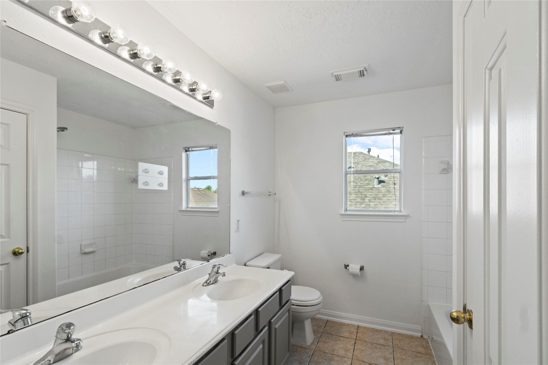 Double-sink vanity bath with tub/shower combo, tile floors, and bright natural light, conveniently located between bedrooms 3 and 4.