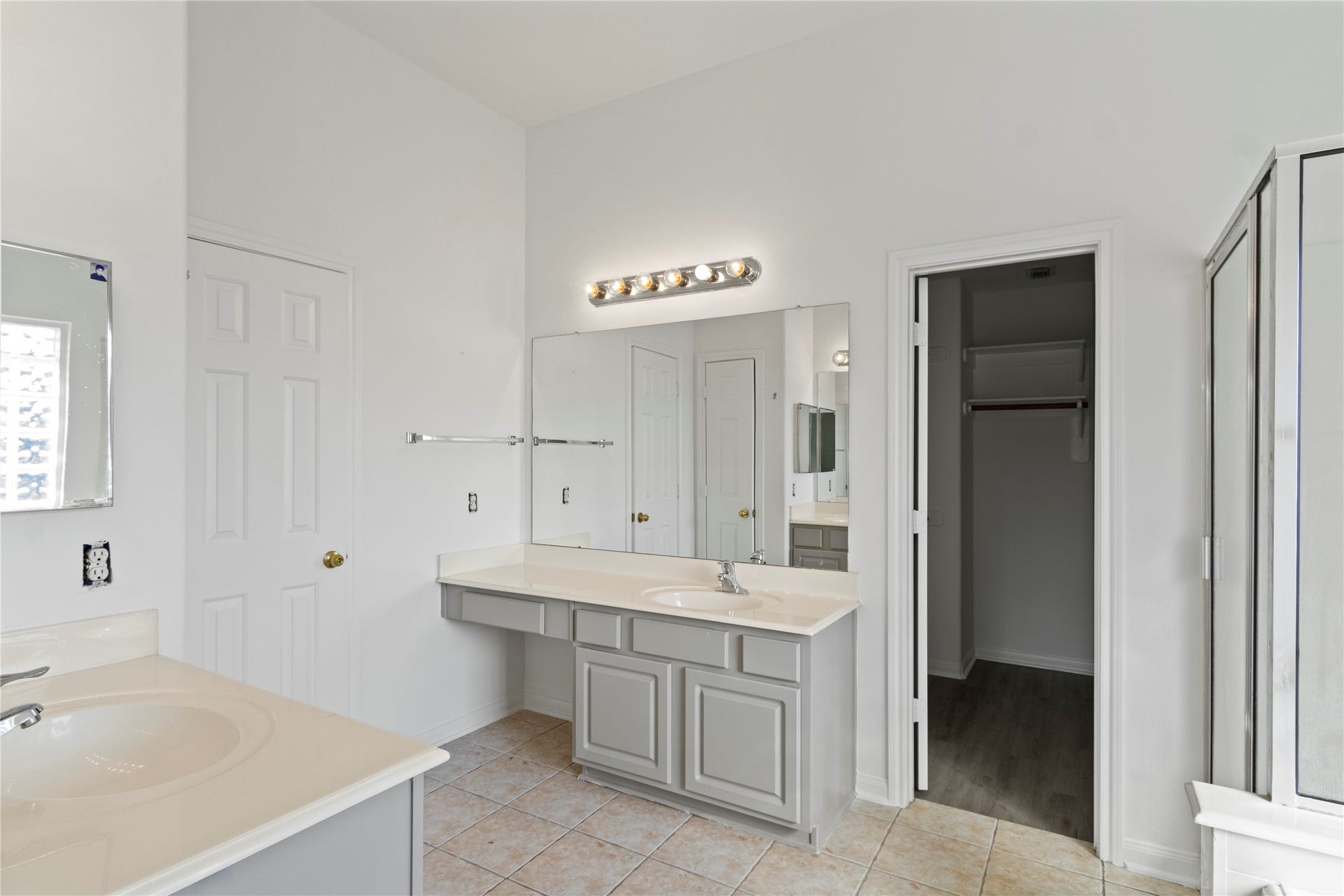 Spacious primary bathroom featuring dual vanities, expansive mirrors, and a walk-in shower, offering a functional layout and neutral finishes.