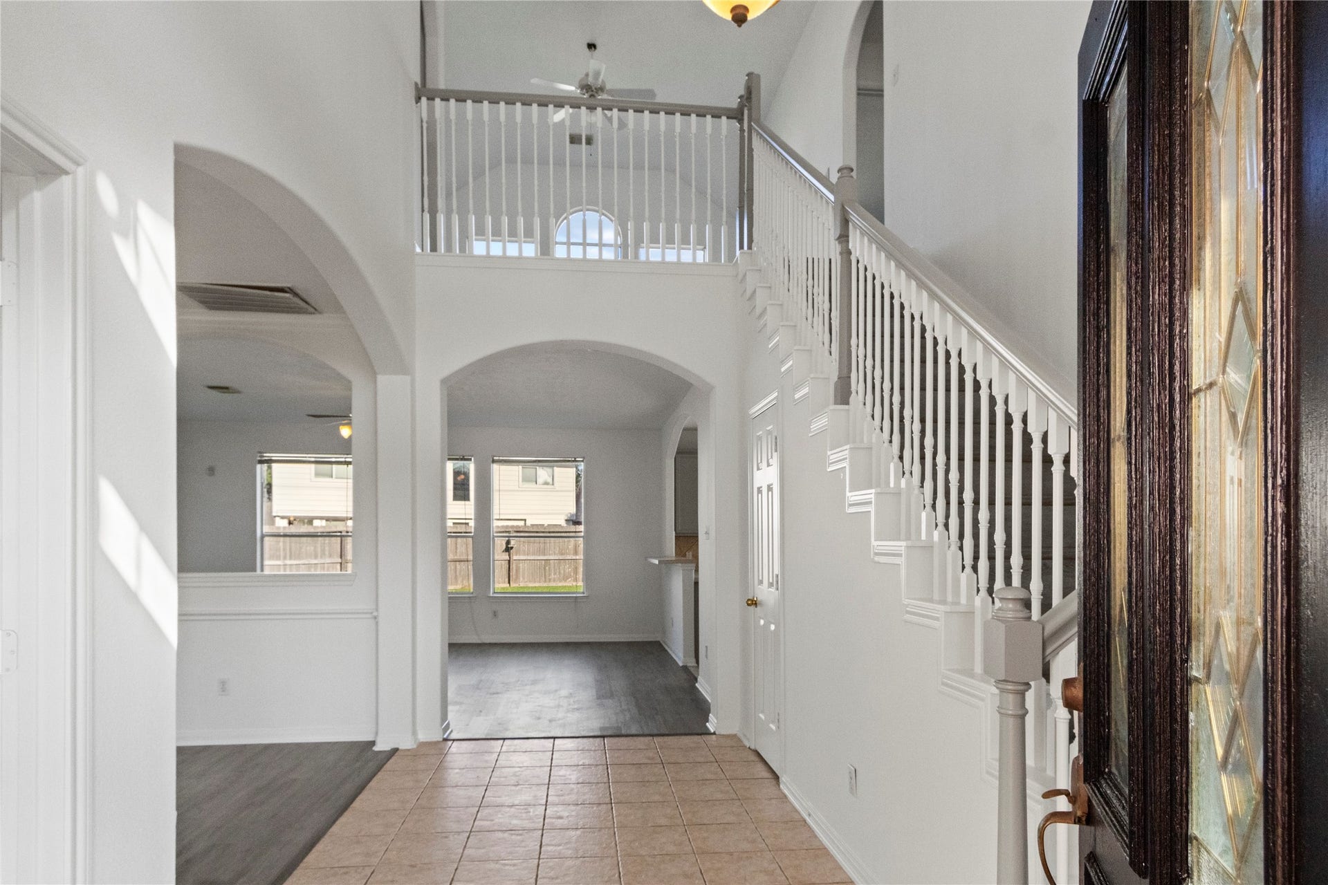 Welcoming two-story entry featuring tile flooring, a staircase with white railings, decorative wall trim, and arched openings leading to the main living areas. The open layout provides a view of the upper-level landing and adjacent living spaces.