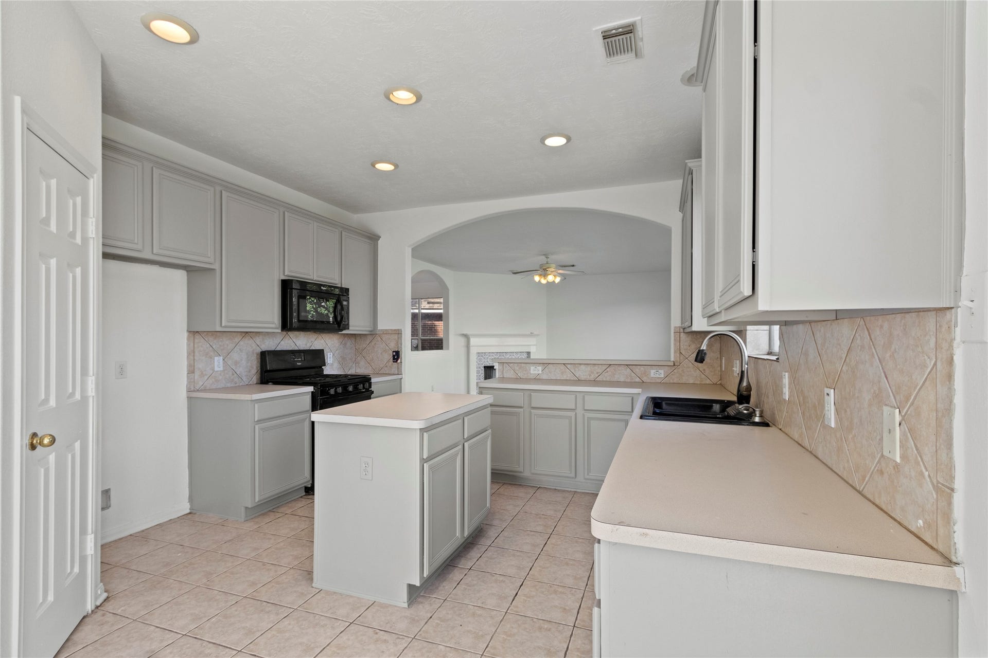 Bright kitchen featuring ample cabinetry, generous counter space, a center island, gas range, and tile flooring. Open archway connects to the adjoining living area.