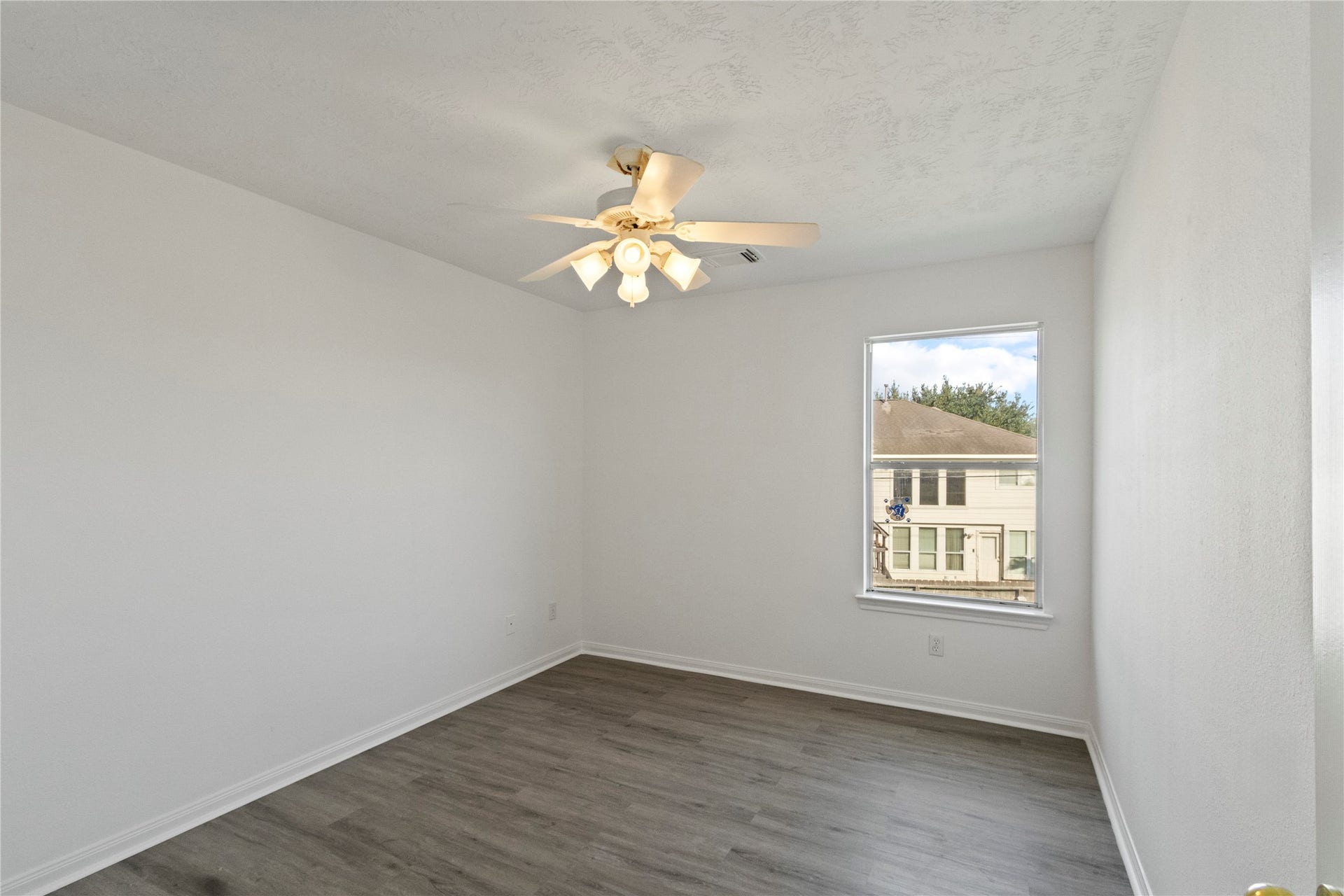 Bedroom 3 features modern gray flooring, a ceiling fan, and a window providing natural light in a bright, neutral space.