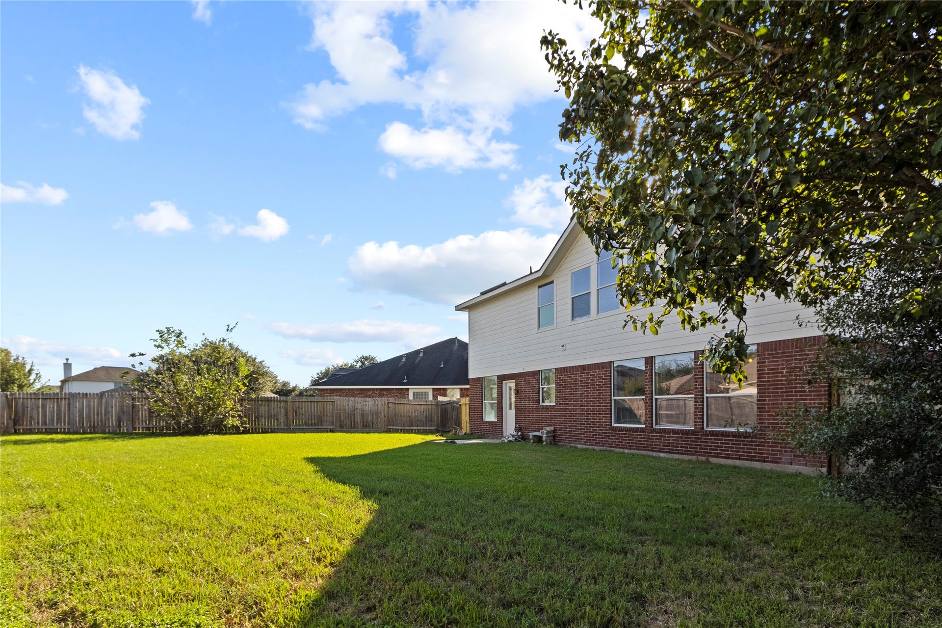Generous fenced backyard with established shade trees and lawn, showcasing the brick two-story elevation and abundant rear and side windows.