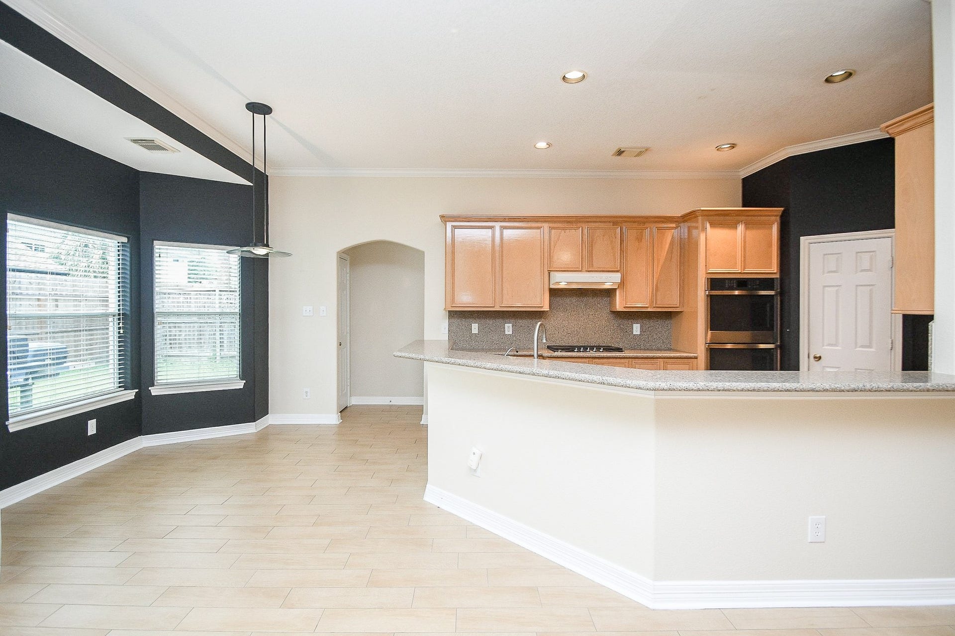 This bright kitchen features light wood cabinetry, a spacious granite countertop with a breakfast bar, and recessed lighting. The open layout connects to a dining area with large windows, providing ample natural light.