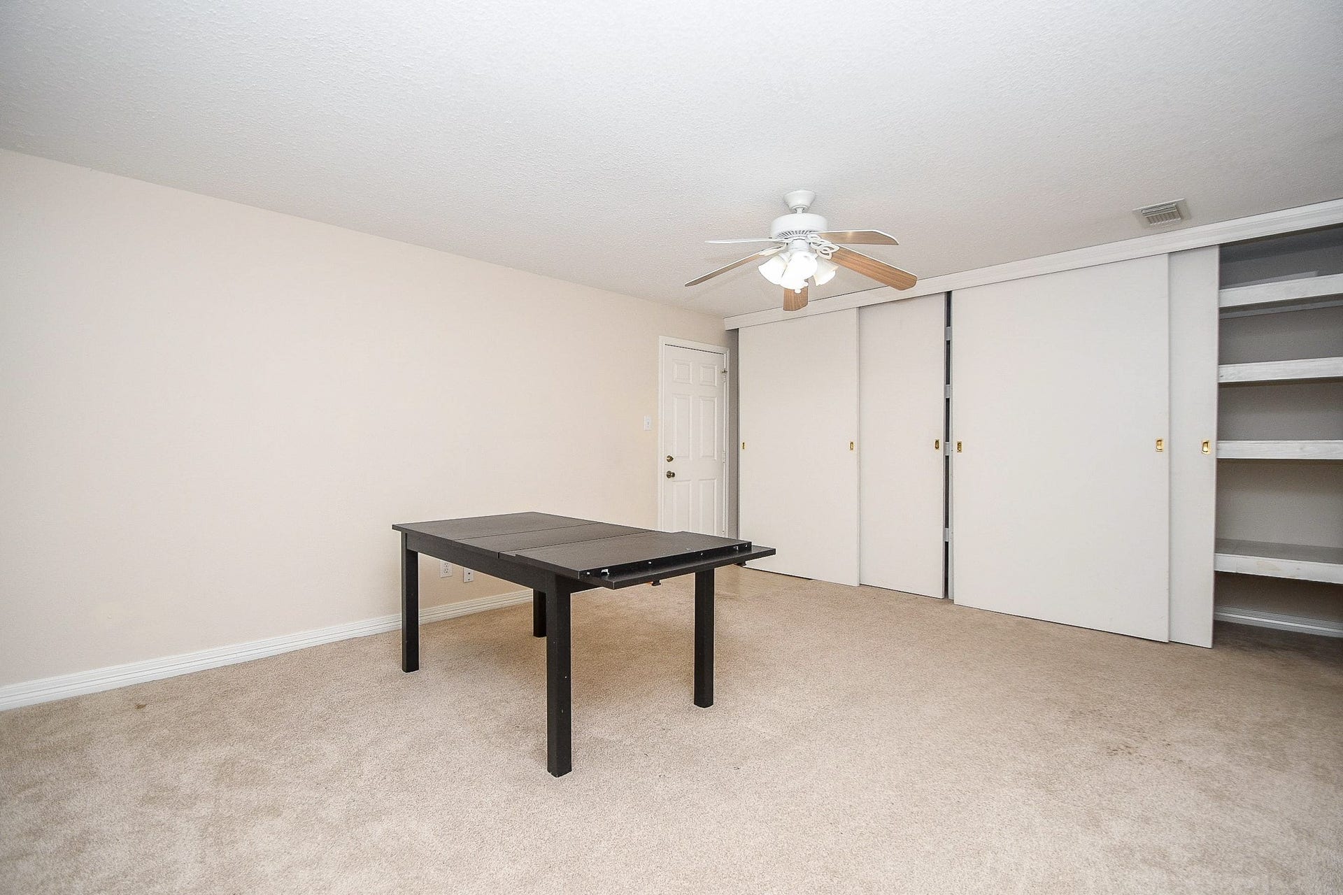 Spacious room with neutral-colored walls and carpet, featuring a ceiling fan and built-in closets with sliding doors. Ideal for a game or hobby room.